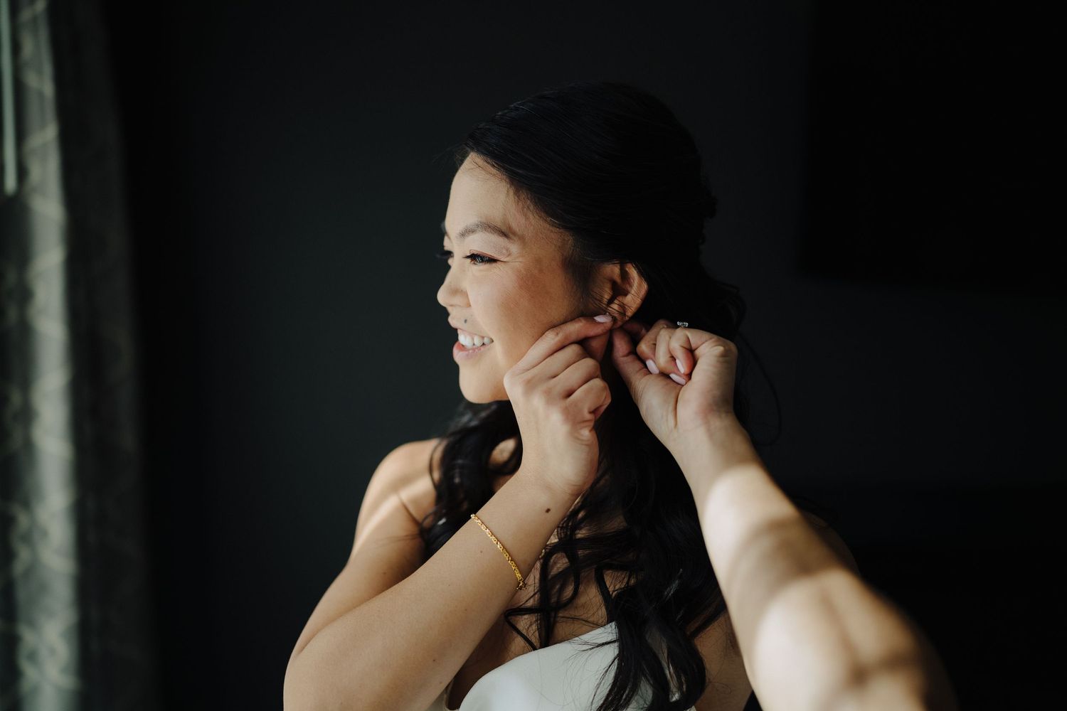 A person puts on earrings in an intimate getting ready moment with moody lighting.