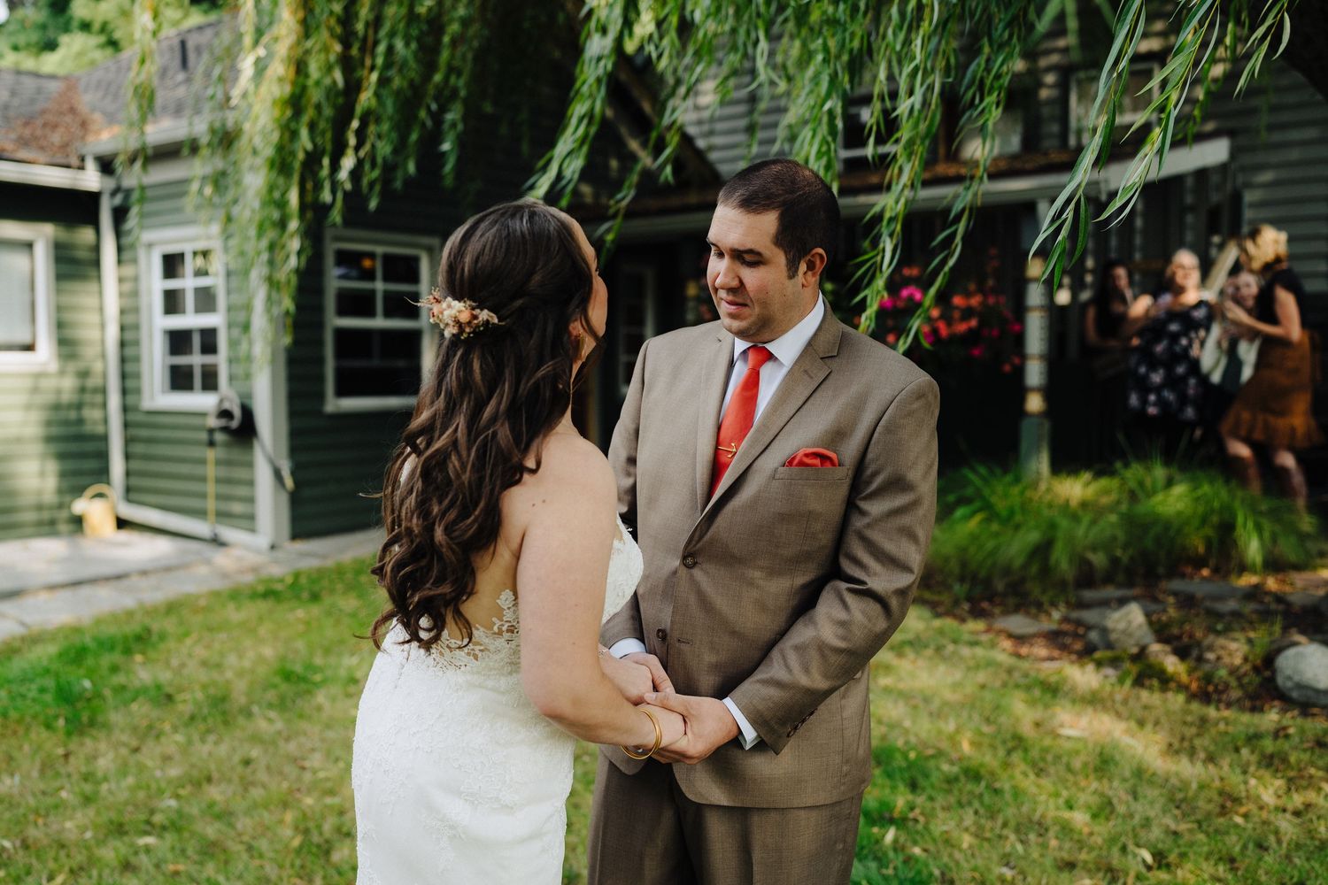 A couple shares an intimate moment during their backyard wedding ceremony while musicians play in the background.