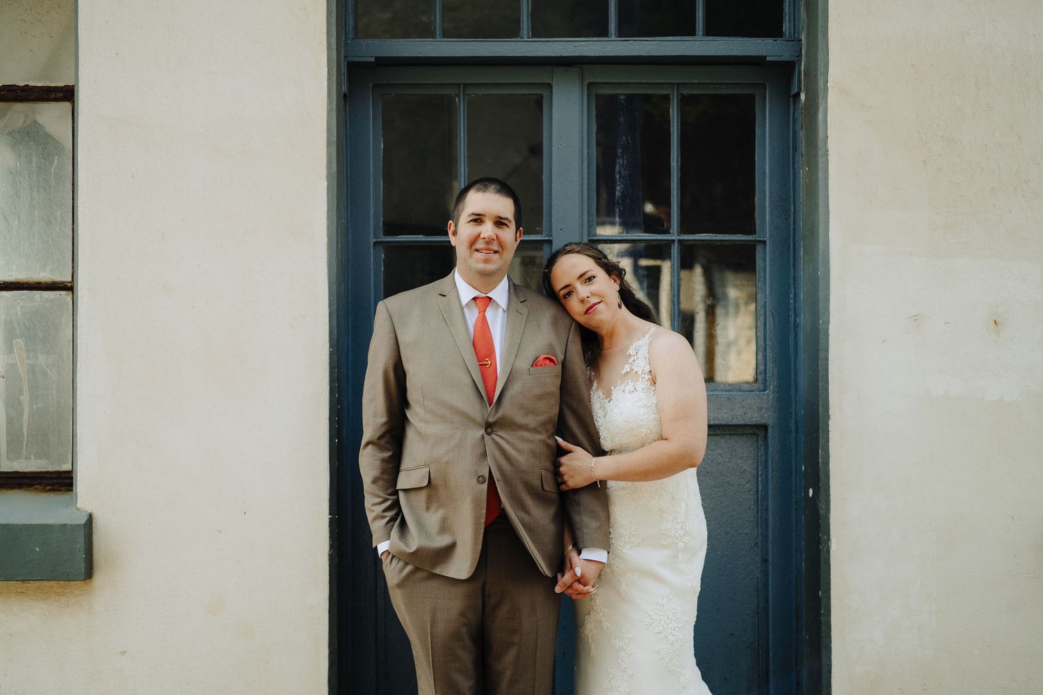 A couple stands in a doorway wearing formal wedding attire.