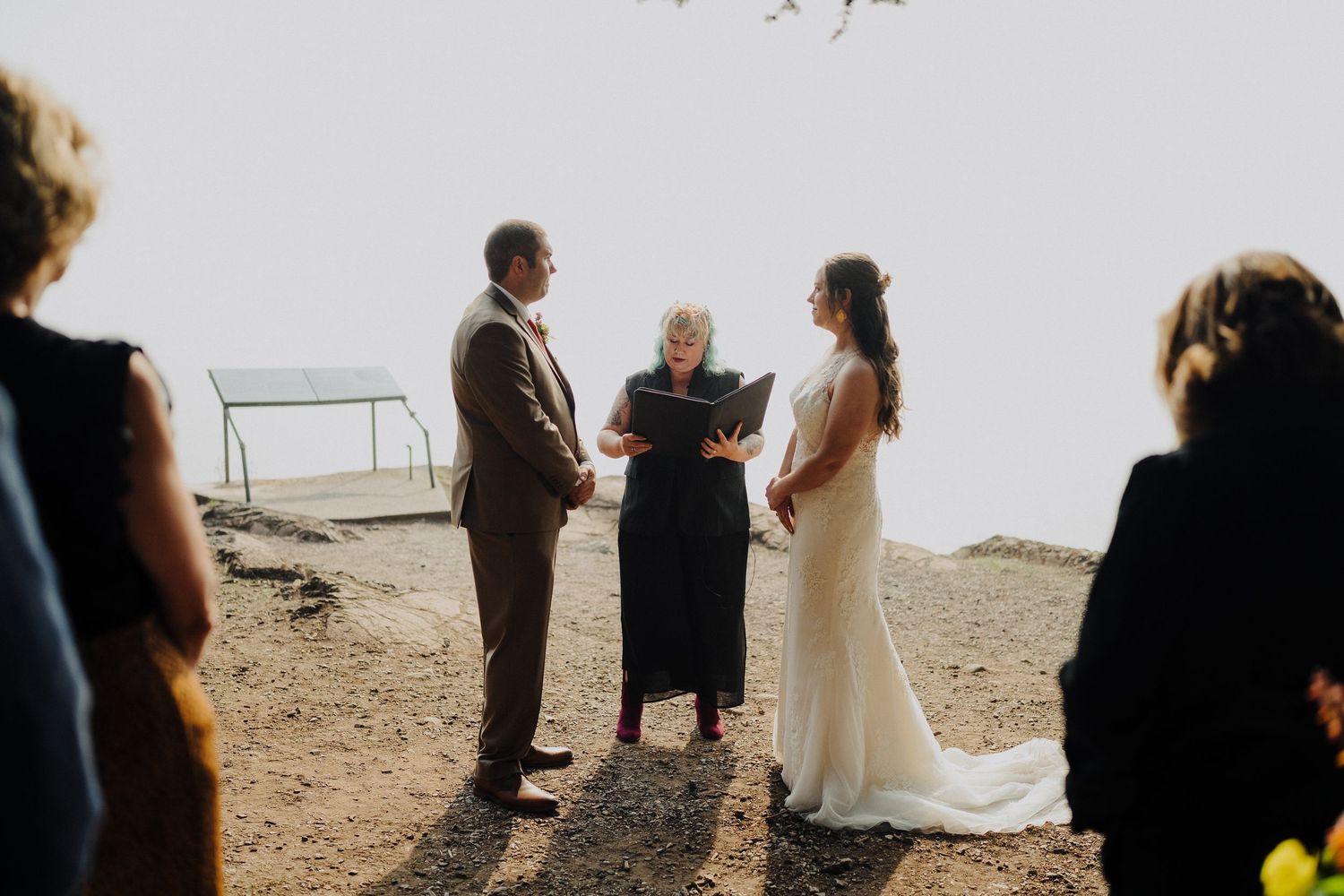 An intimate outdoor beach wedding ceremony takes place on a cliff overlooking the ocean at sunset.