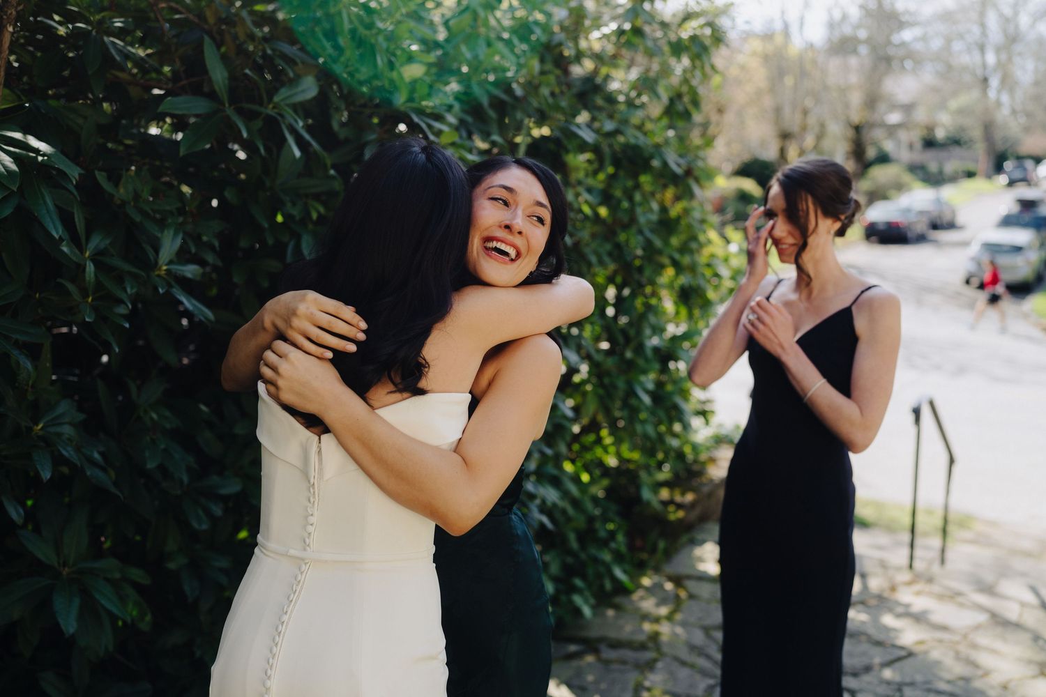 Two figures embrace while another reacts with joy during an emotional outdoor gathering.