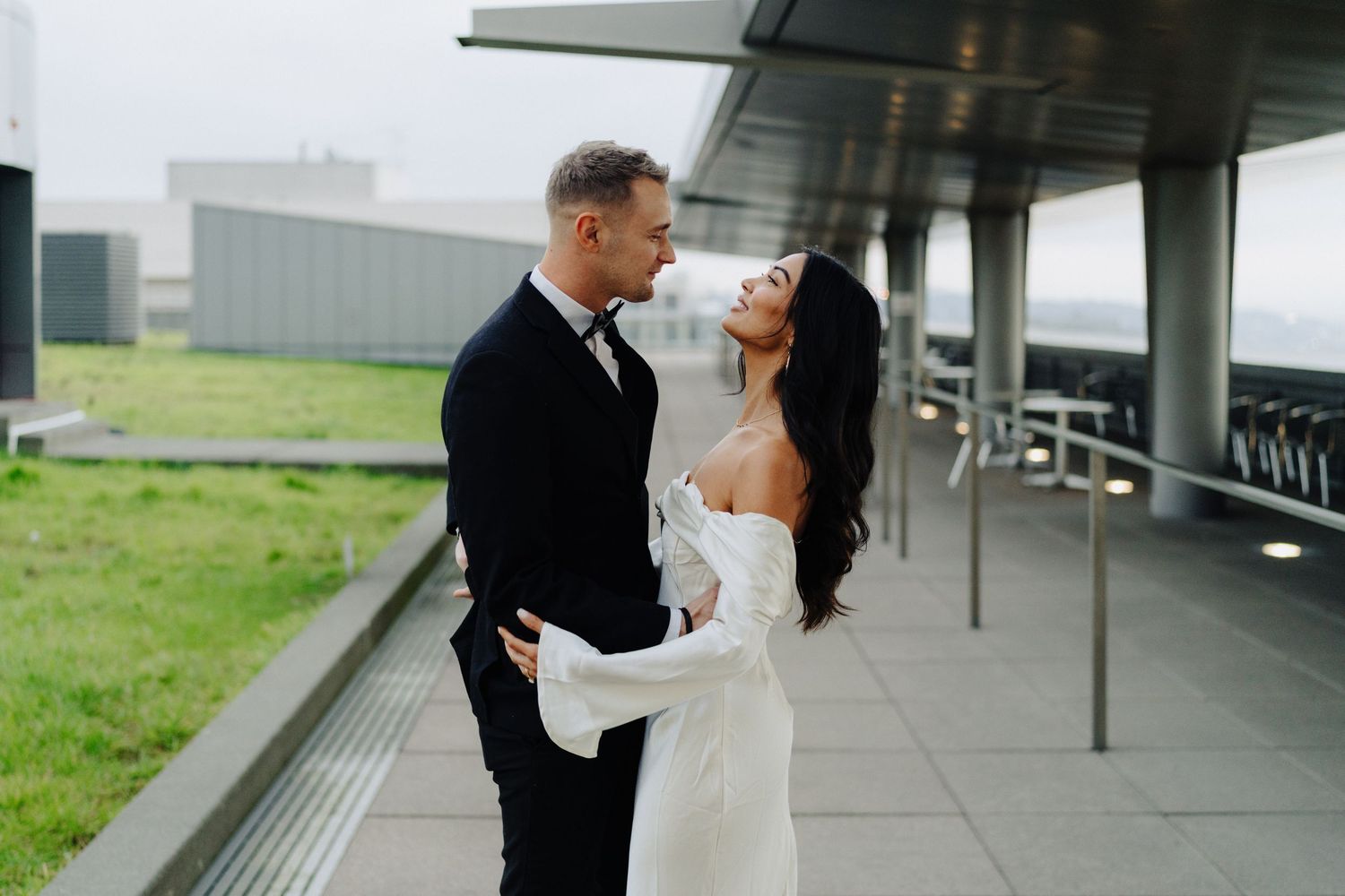 A couple in wedding attire shares a joyful moment on an outdoor terrace.