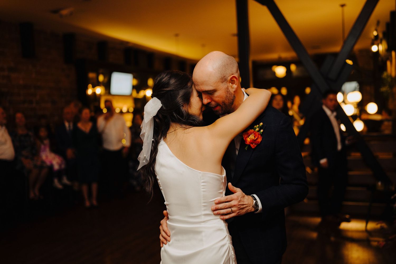 Couple sharing an intimate dance moment during wedding reception in dimly lit venue.