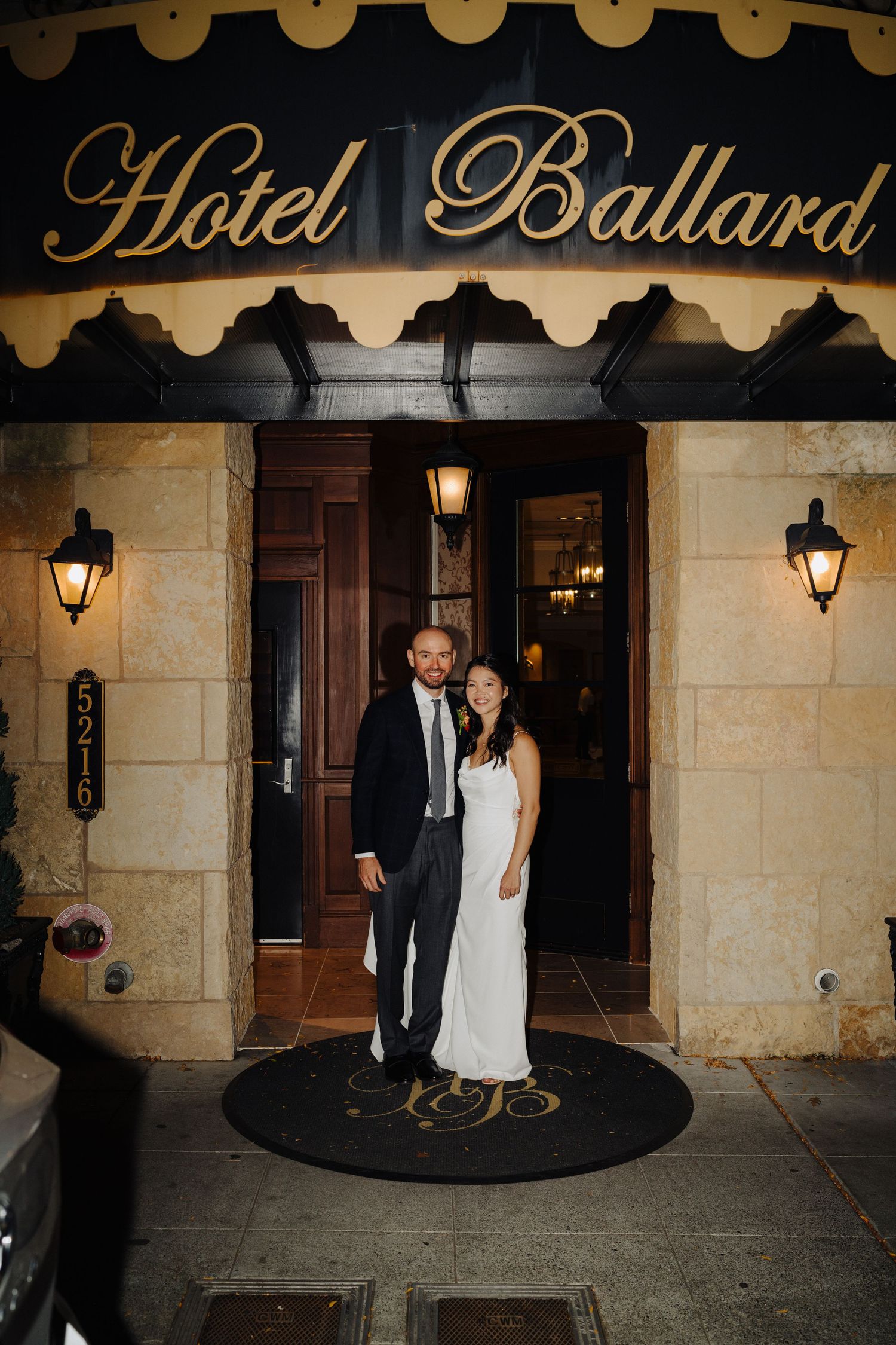 Elegant couple standing at entrance of Hotel Ballard with illuminated vintage signage above.