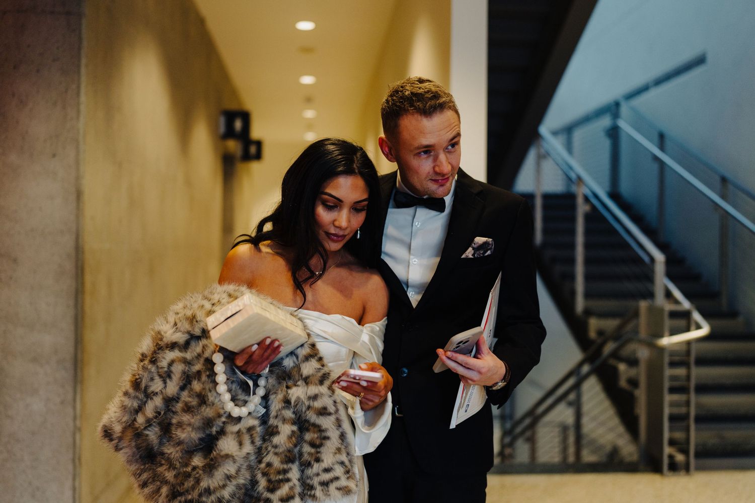 A couple looking at a phone together in an elegant hallway setting.