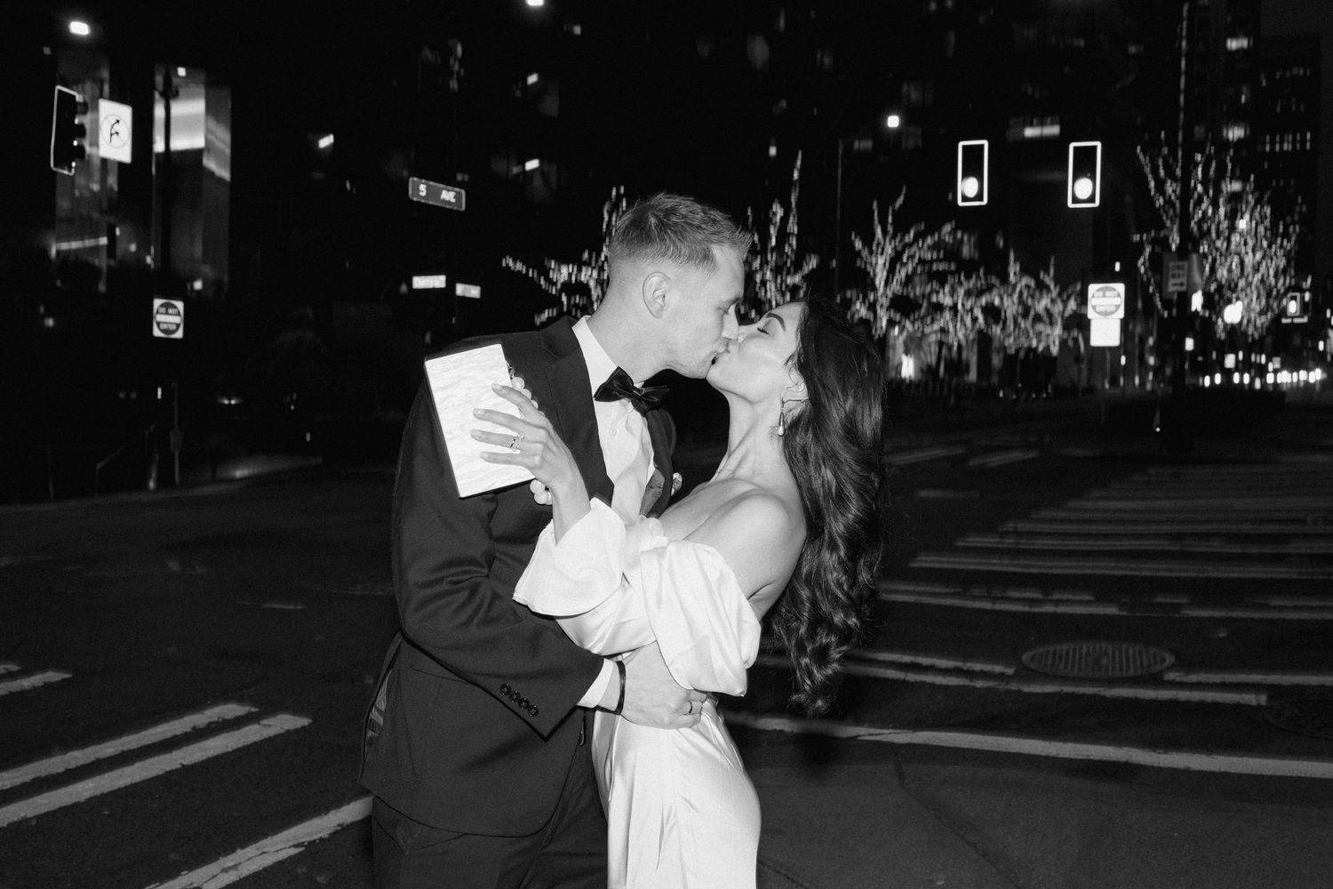 Black and white nighttime portrait of newlyweds embracing on a city street.