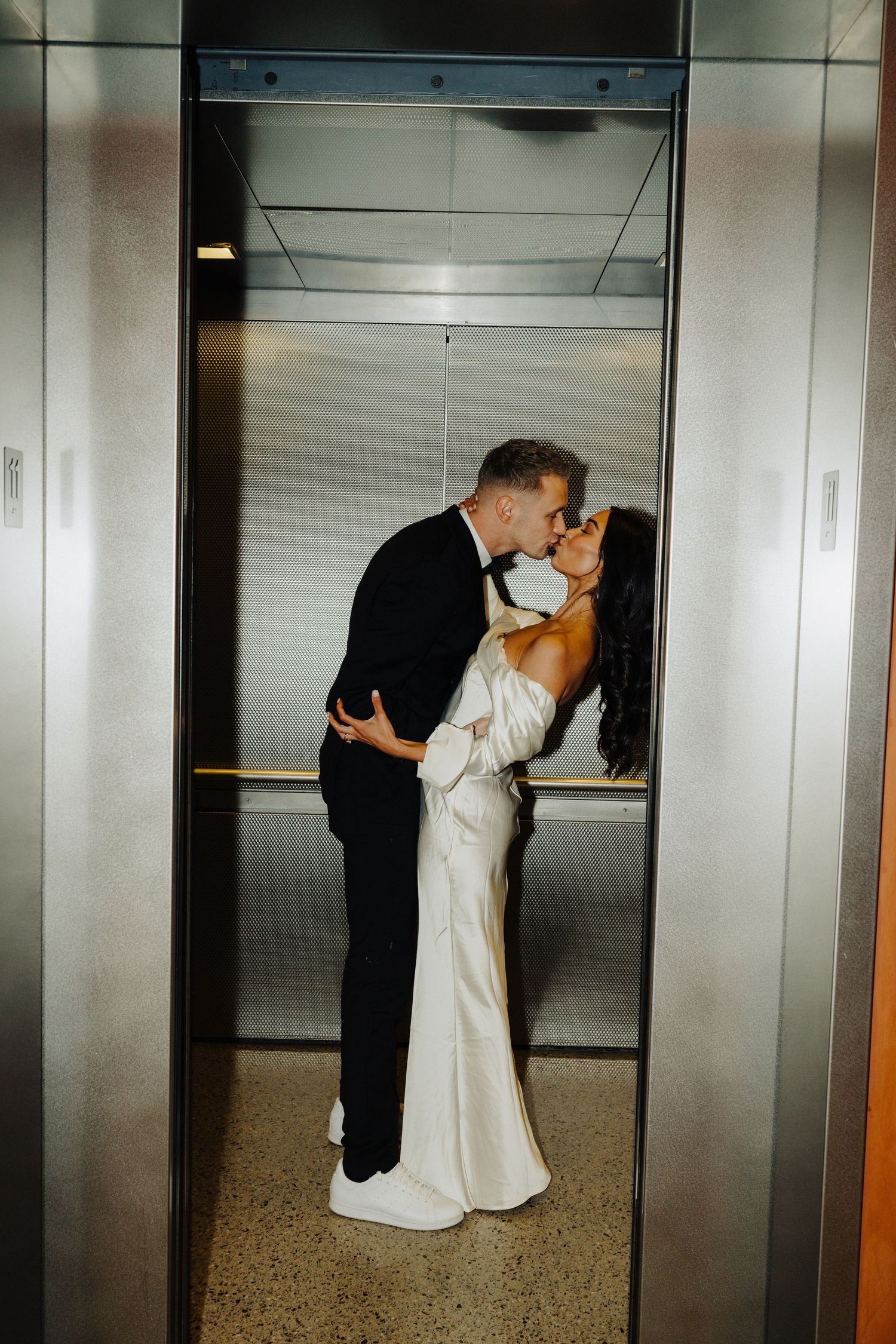 Romantic wedding photo of couple sharing tender moment in modern elevator in formal attire.