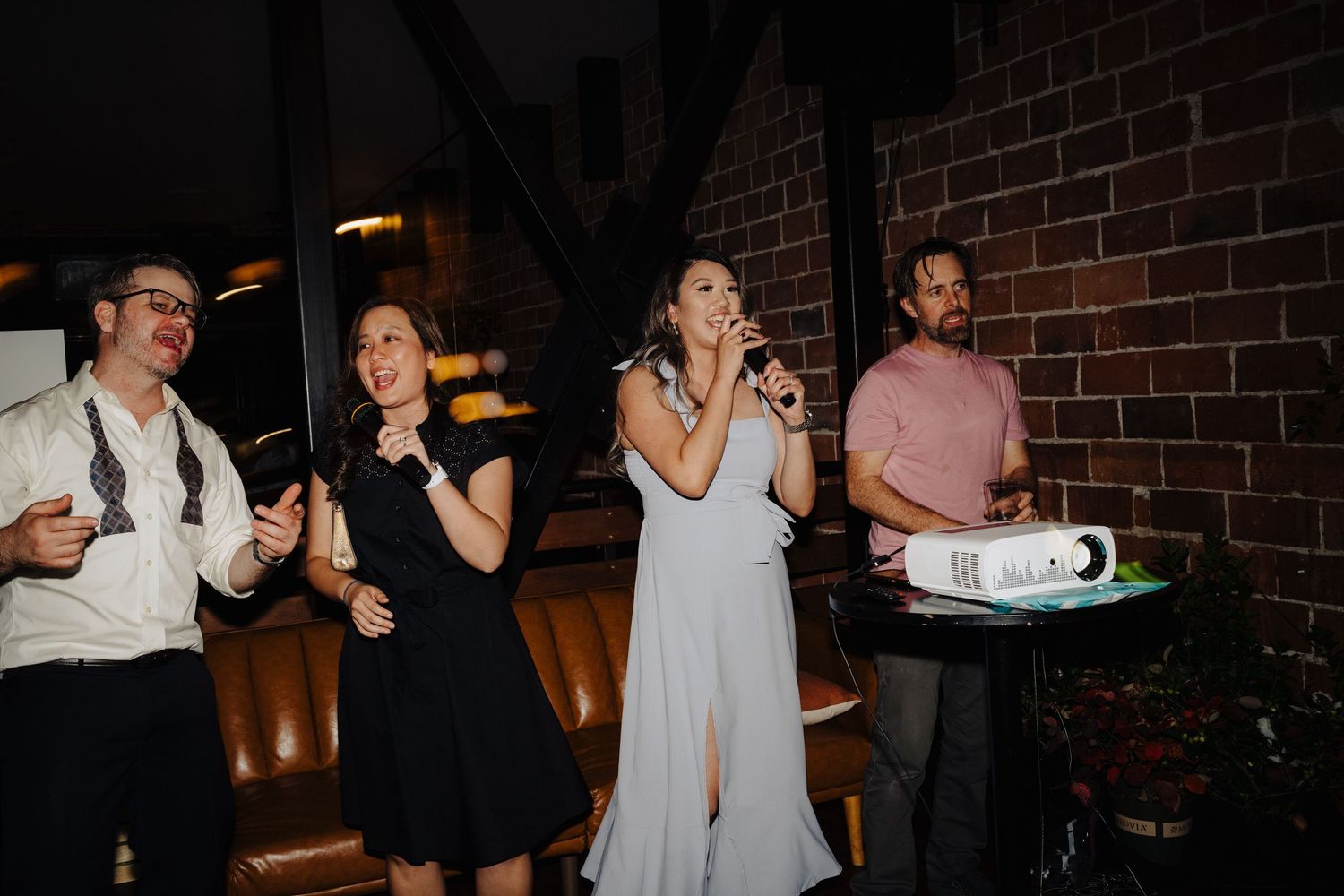 Wedding guests singing and celebrating at reception venue with exposed brick walls.