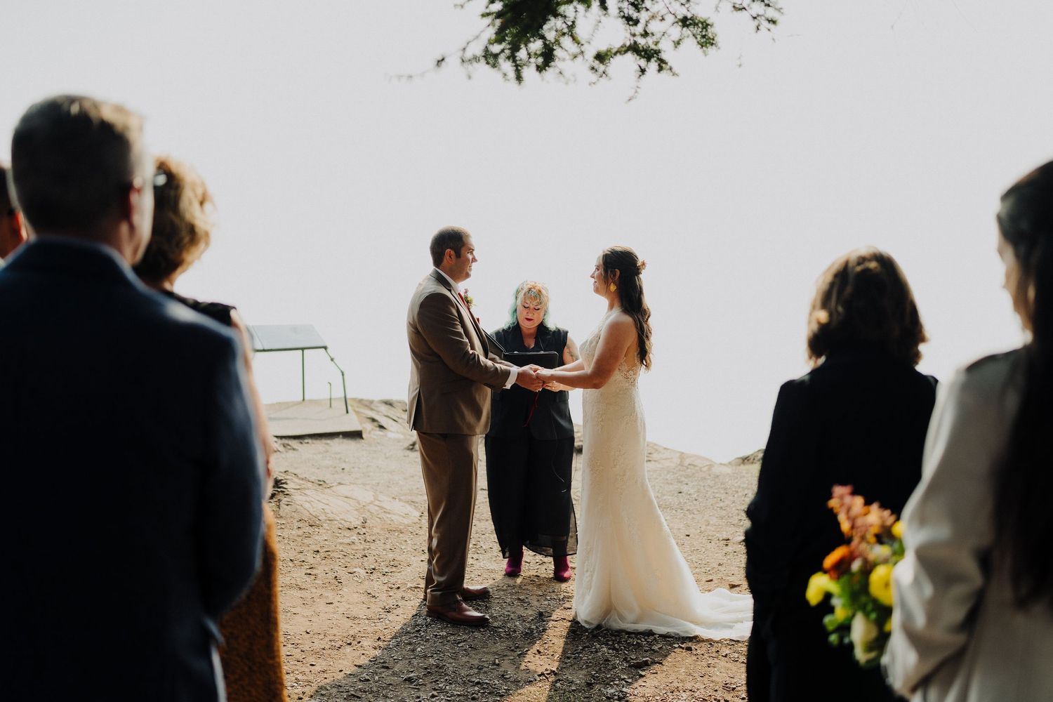 A small wedding ceremony unfolds on a scenic cliff overlooking a misty landscape.