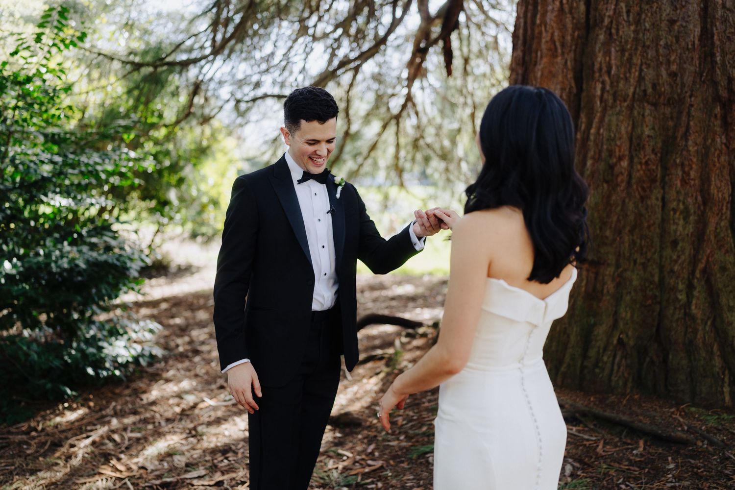 A couple in wedding attire sharing a romantic moment under trees in an outdoor setting.