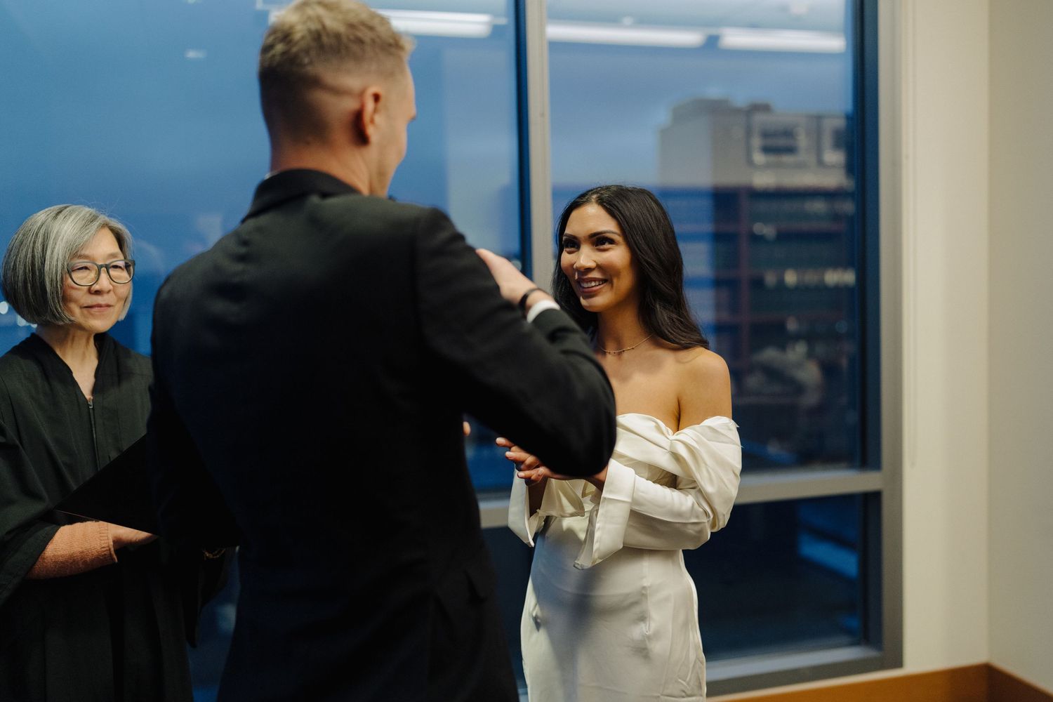 A wedding ceremony takes place in an office space with large windows overlooking the city.