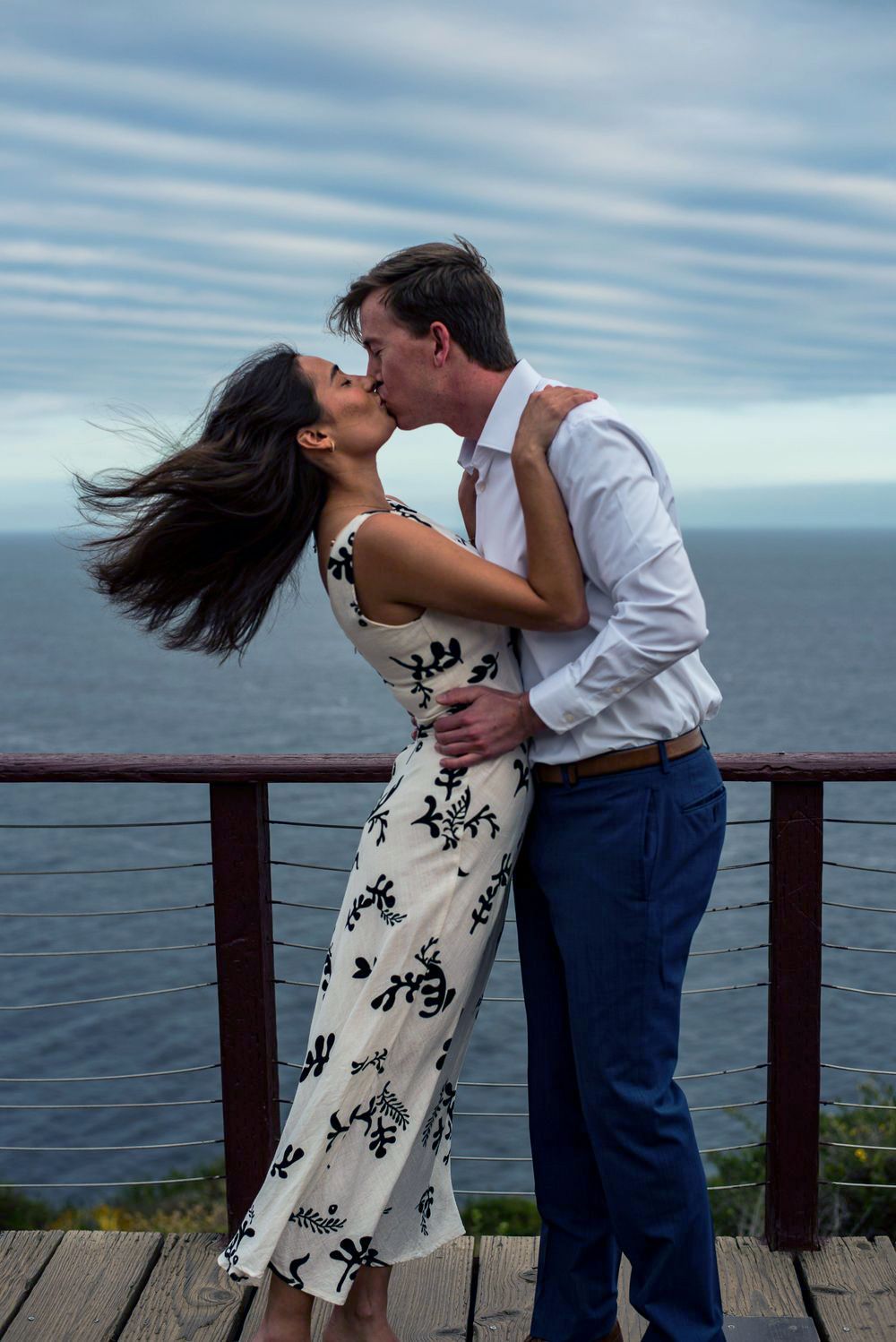 Malibu CA,, engagement photo of couple kissing on an oceanfront cliff deck, captured in natural light with coastal views.