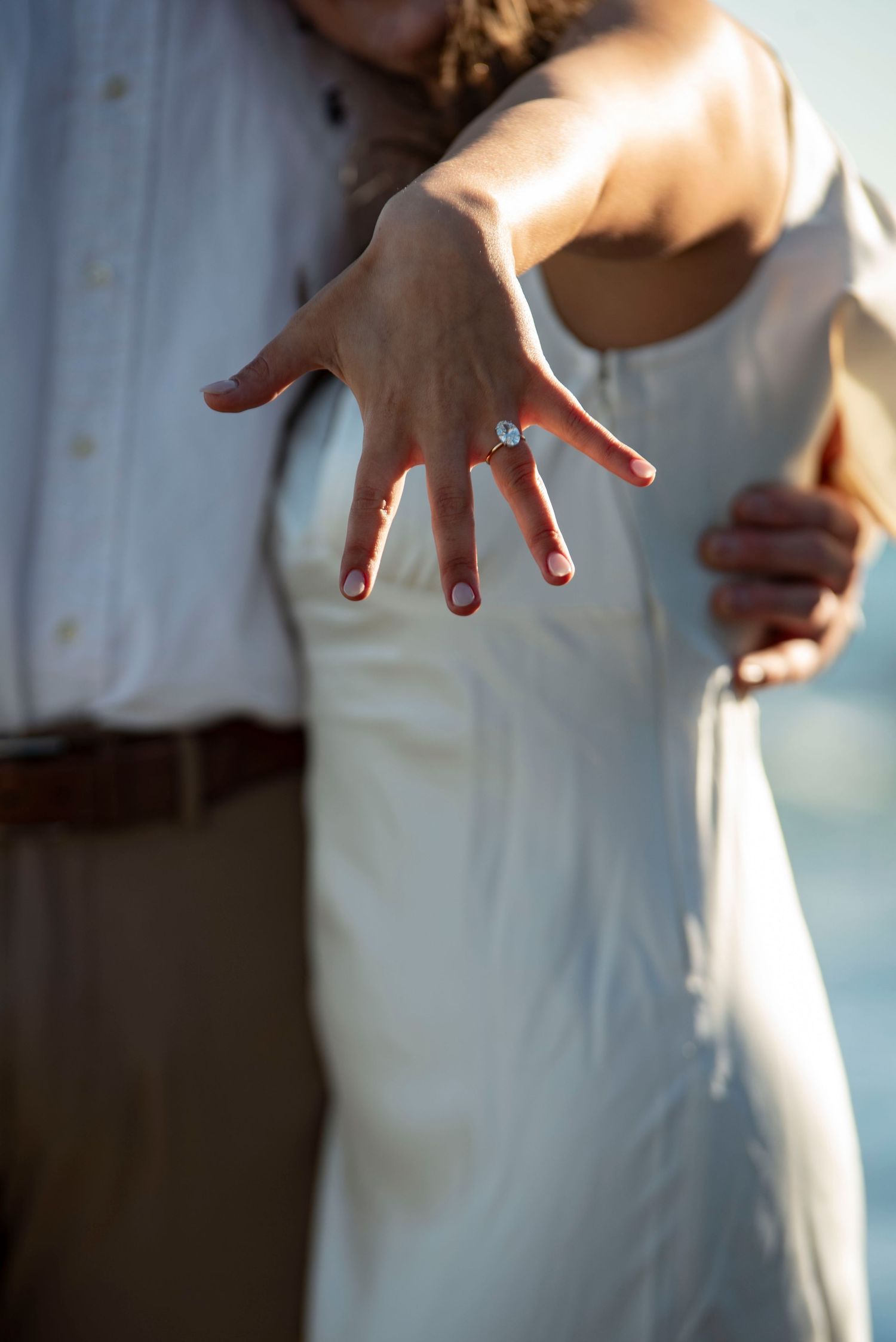 Close-up of a raised hand with an engagement ring, lit by warm golden light, capturing a candid post-proposal moment.