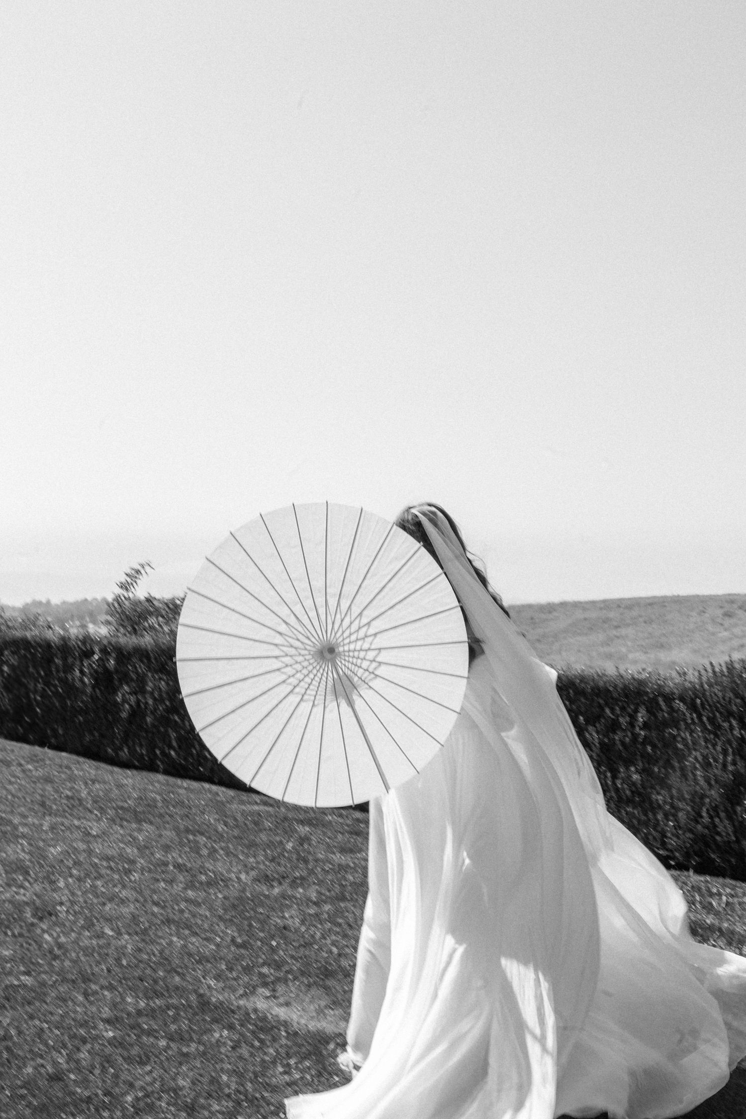 A flowing white wedding dress and parasol create an artistic silhouette against a misty horizon. Documentary photographer