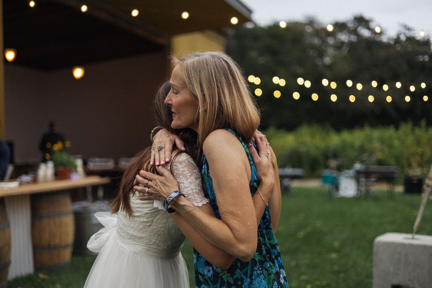 Two people share an emotional embrace at an outdoor evening event with string lights Documentary photographer