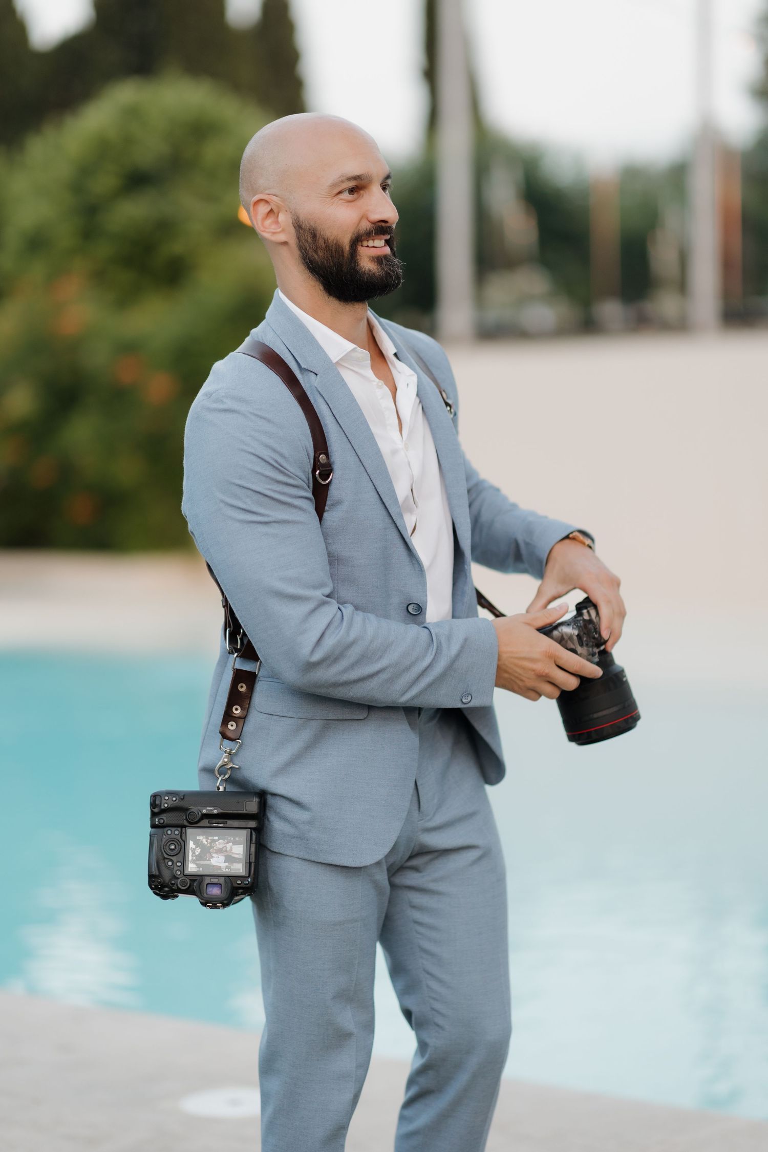 Professional photographer in light blue suit with camera standing by poolside at outdoor venue taking photos.