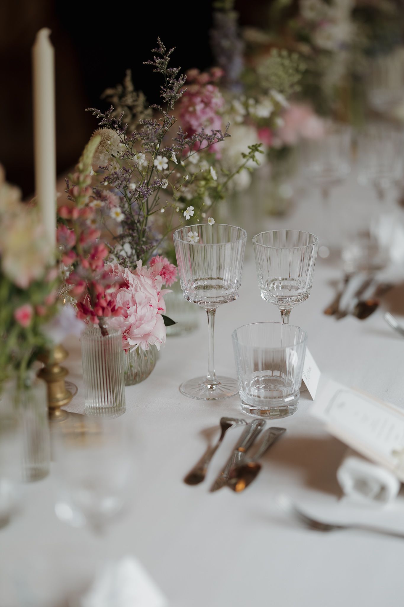 Elegant table settings with crystal glassware and soft pink floral centerpieces create a romantic wedding reception atmosphere.