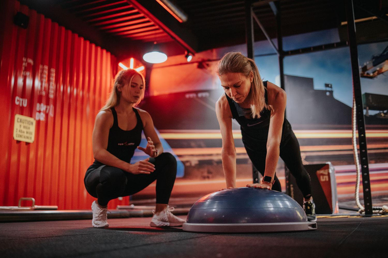 People performing plank exercises in a red-lit gym during a group fitness class.
