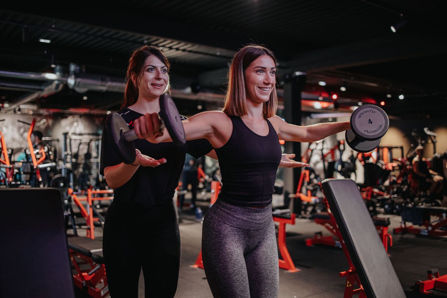 Two energetic people working out together and having fun in a modern gym with exercise equipment in the background.