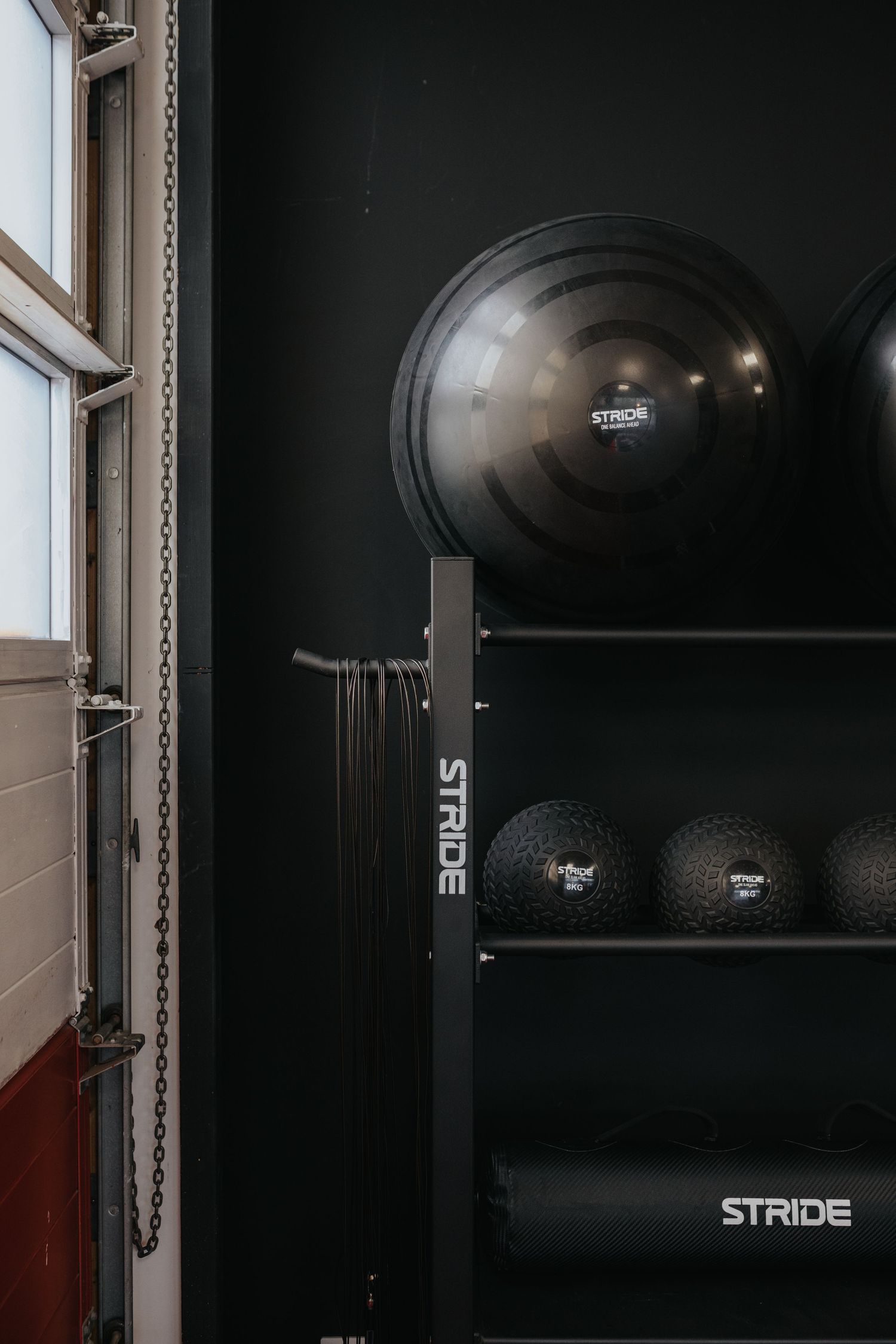 Exercise equipment including black medicine balls and fitness gear arranged on dark shelves next to a bright window.