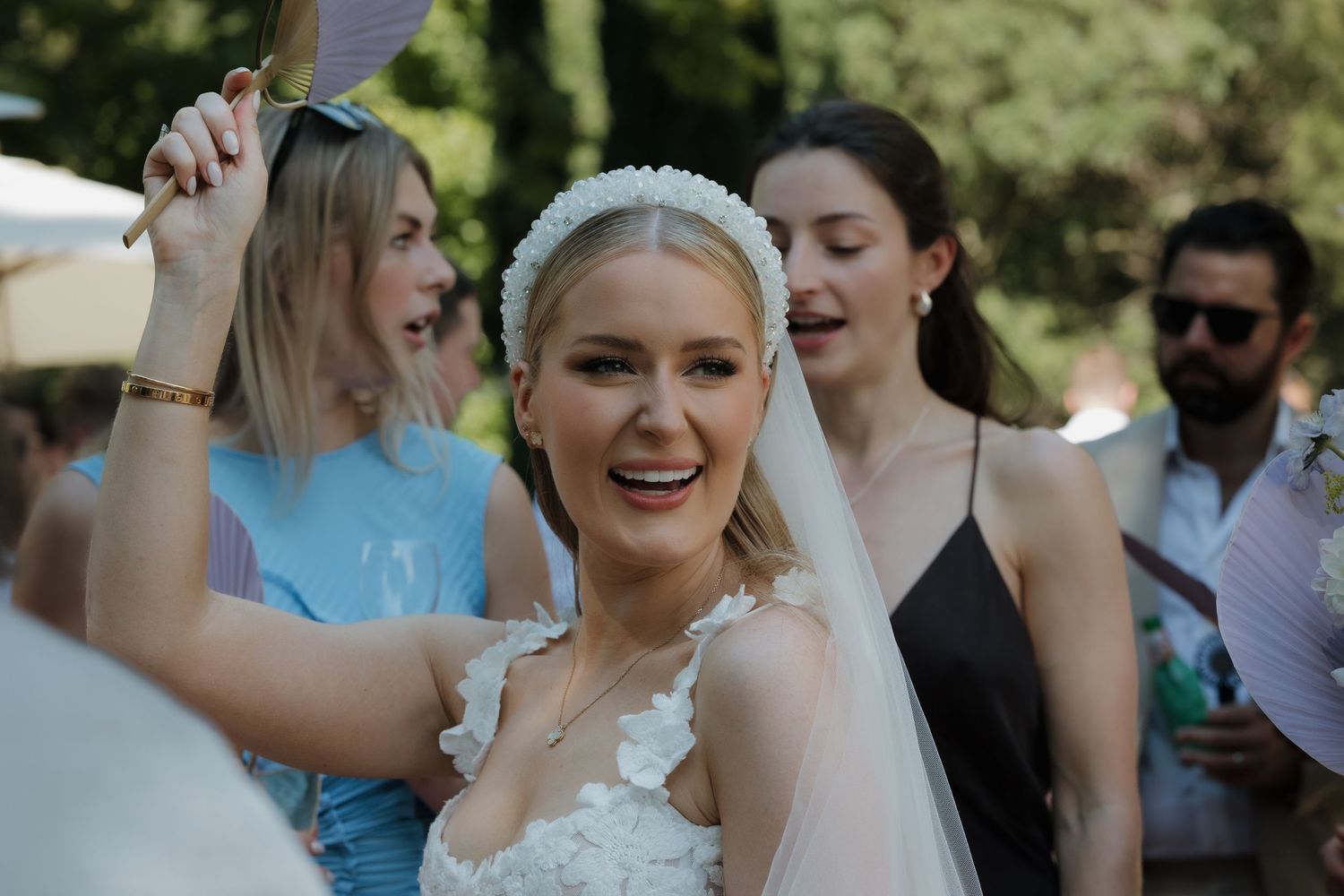 Joyful moment captured at outdoor wedding celebration with bride in white dress and veil surrounded by guests dancing.