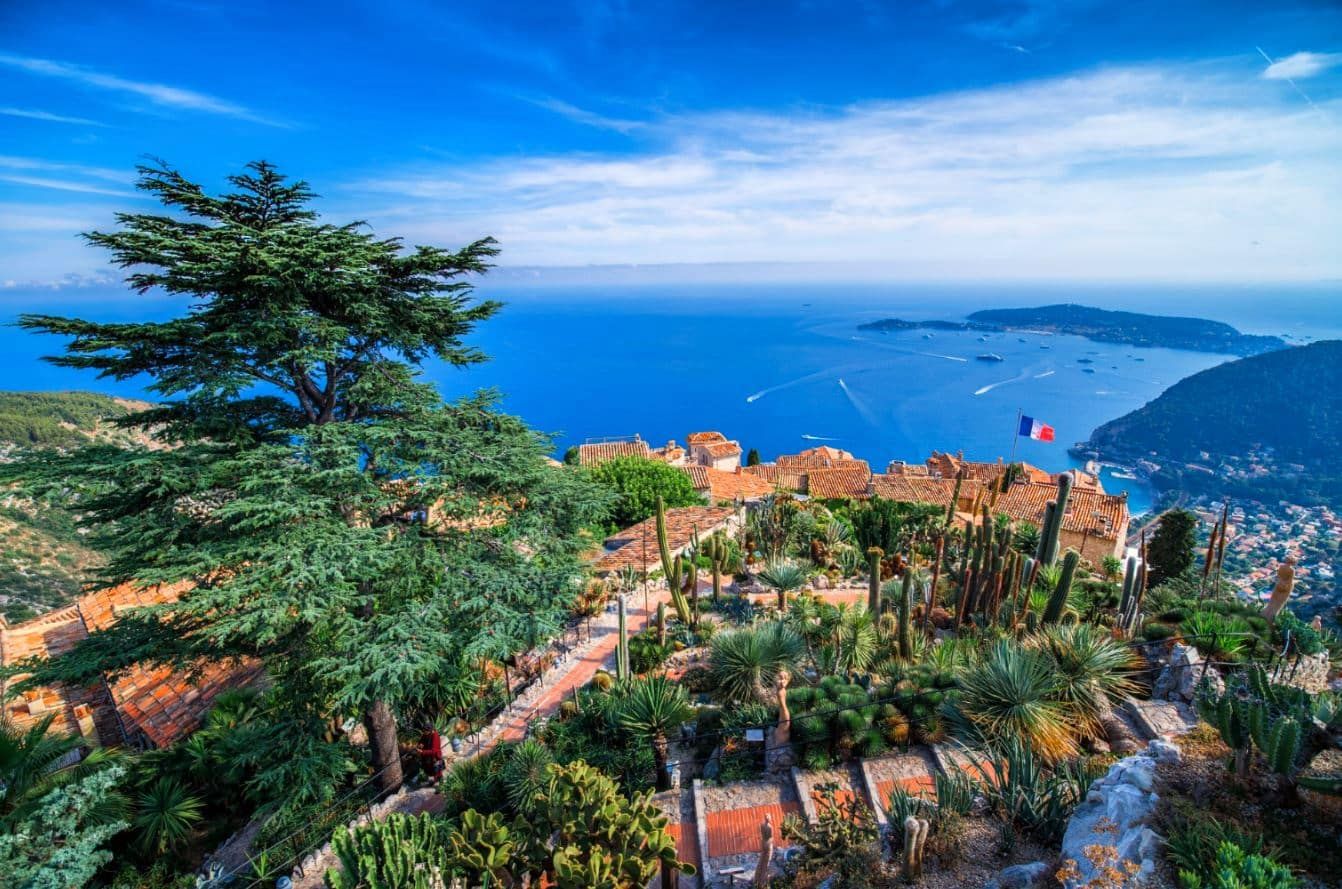 Scenic Mediterranean hillside view of terracotta roofs and blue sea from Eze village in France with cypress trees.