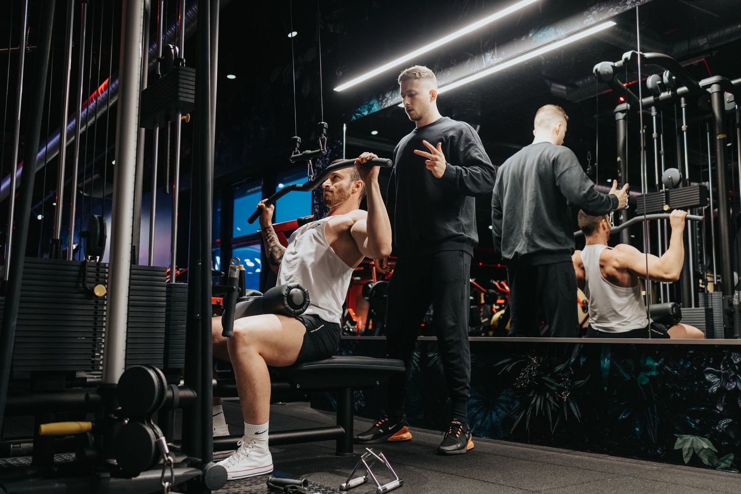 People working out at a modern gym with exercise equipment and bright lighting in dark ambiance setting.