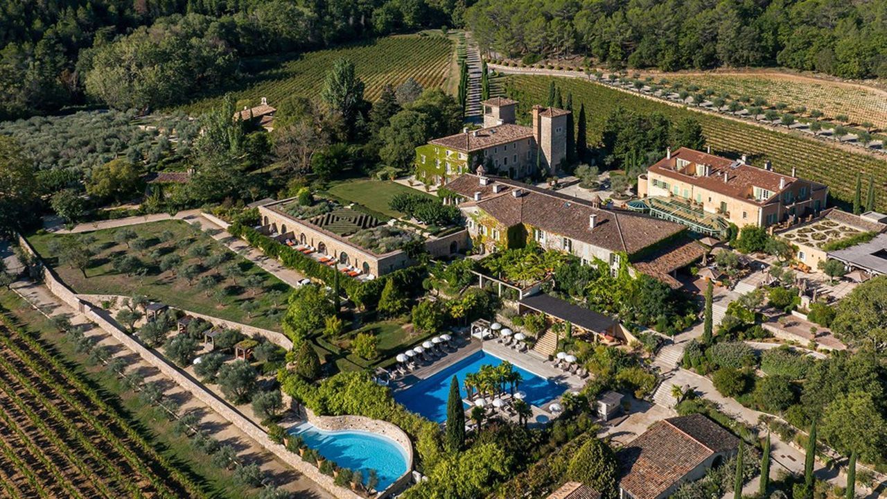 Aerial view of a luxurious Tuscan resort with swimming pools, manicured gardens and rustic villa buildings nestled in countryside.