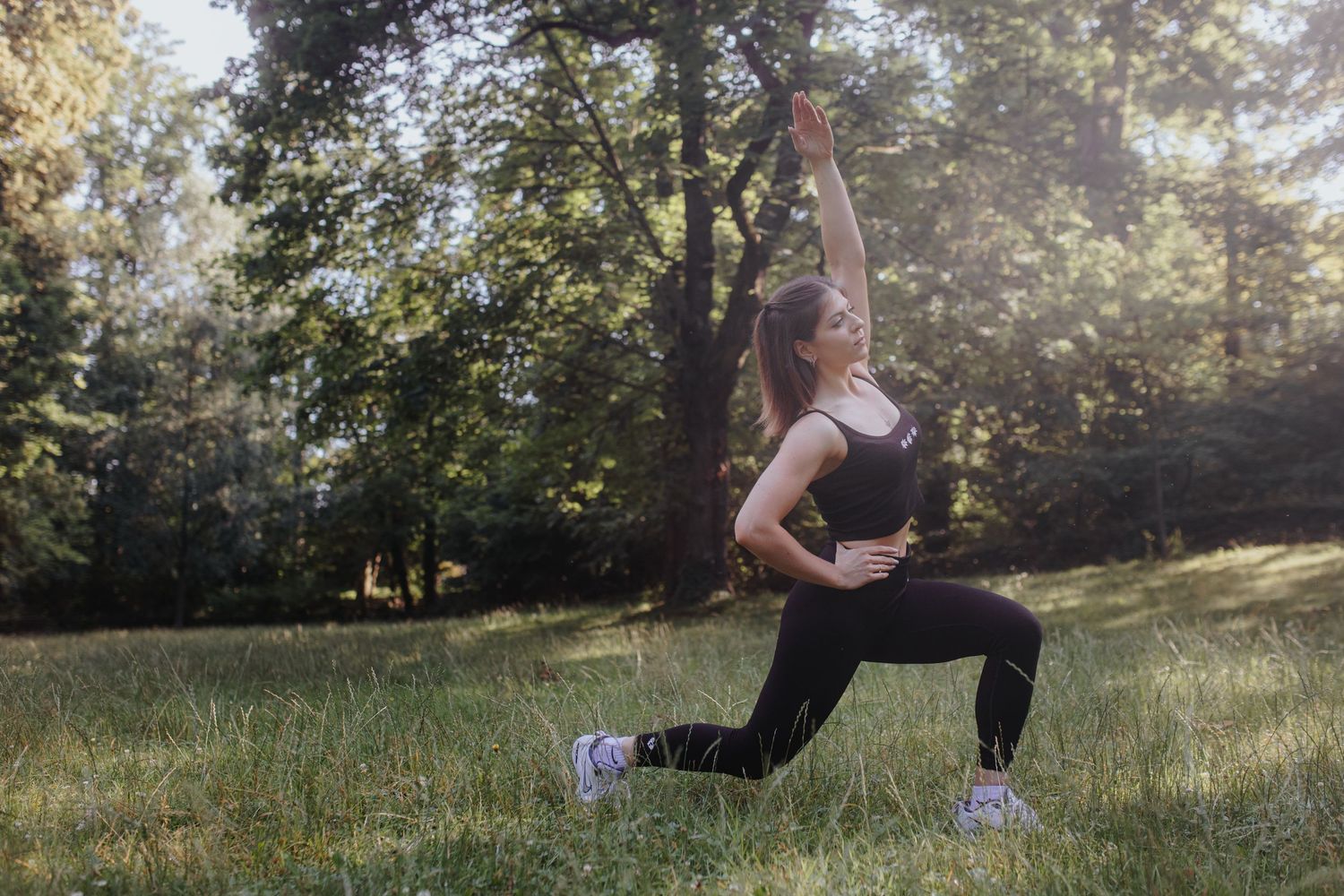 An athlete stretches and warms up in a sunny meadow surrounded by trees during outdoor exercise.