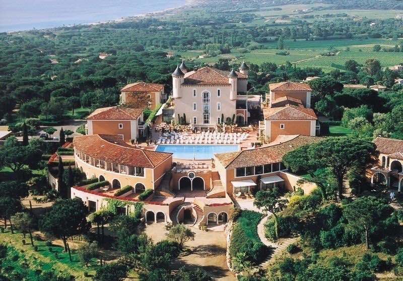 Luxurious Mediterranean resort with terra cotta roofs and swimming pool nestled in lush hillside overlooking scenic countryside.