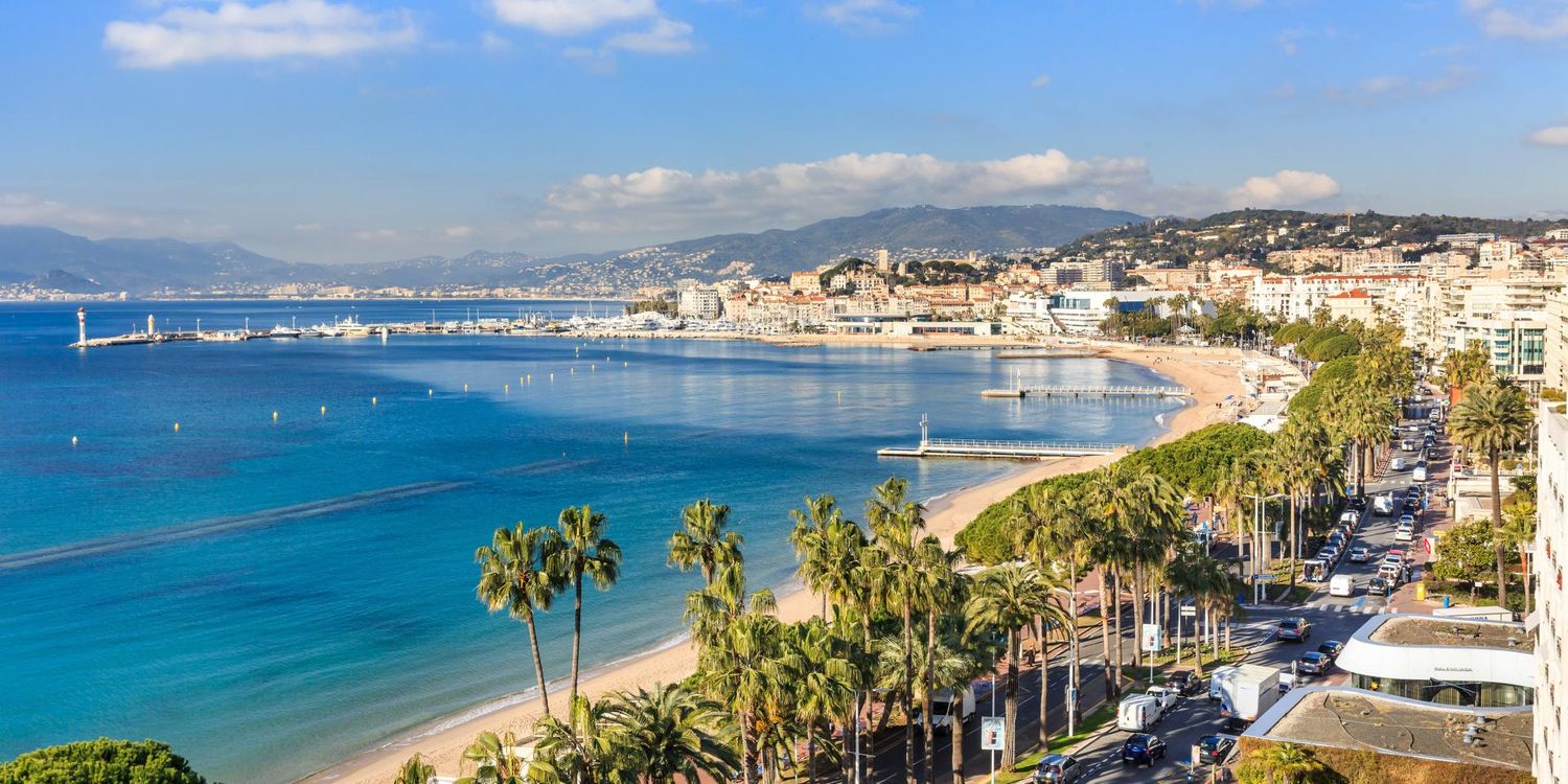 Coastal panorama of Cannes French Riviera with turquoise Mediterranean sea, palm trees and seaside promenade.