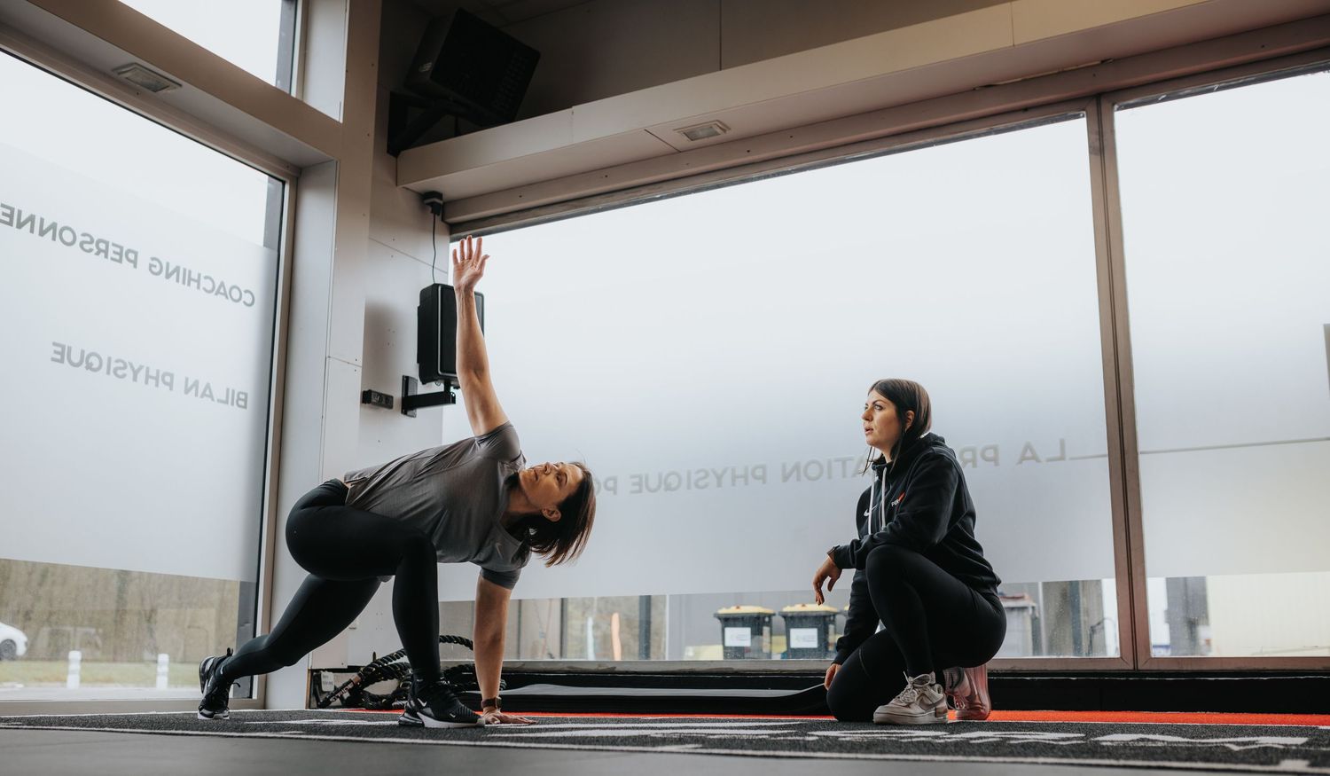 Two people engaging in a fitness workout session using yoga mats in a bright studio space.
