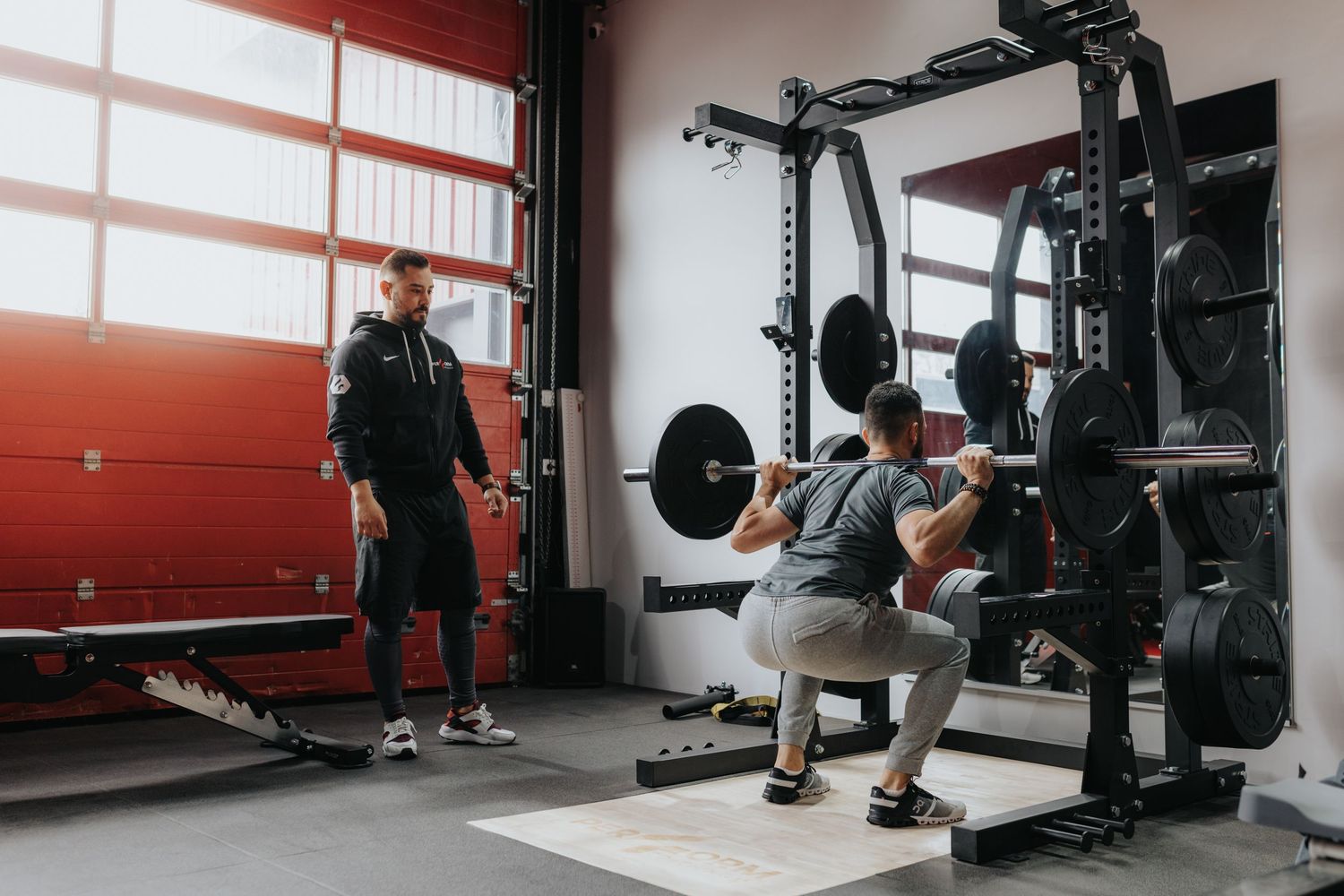 A weightlifting session at a modern gym facility with a power rack and exercise equipment setup.