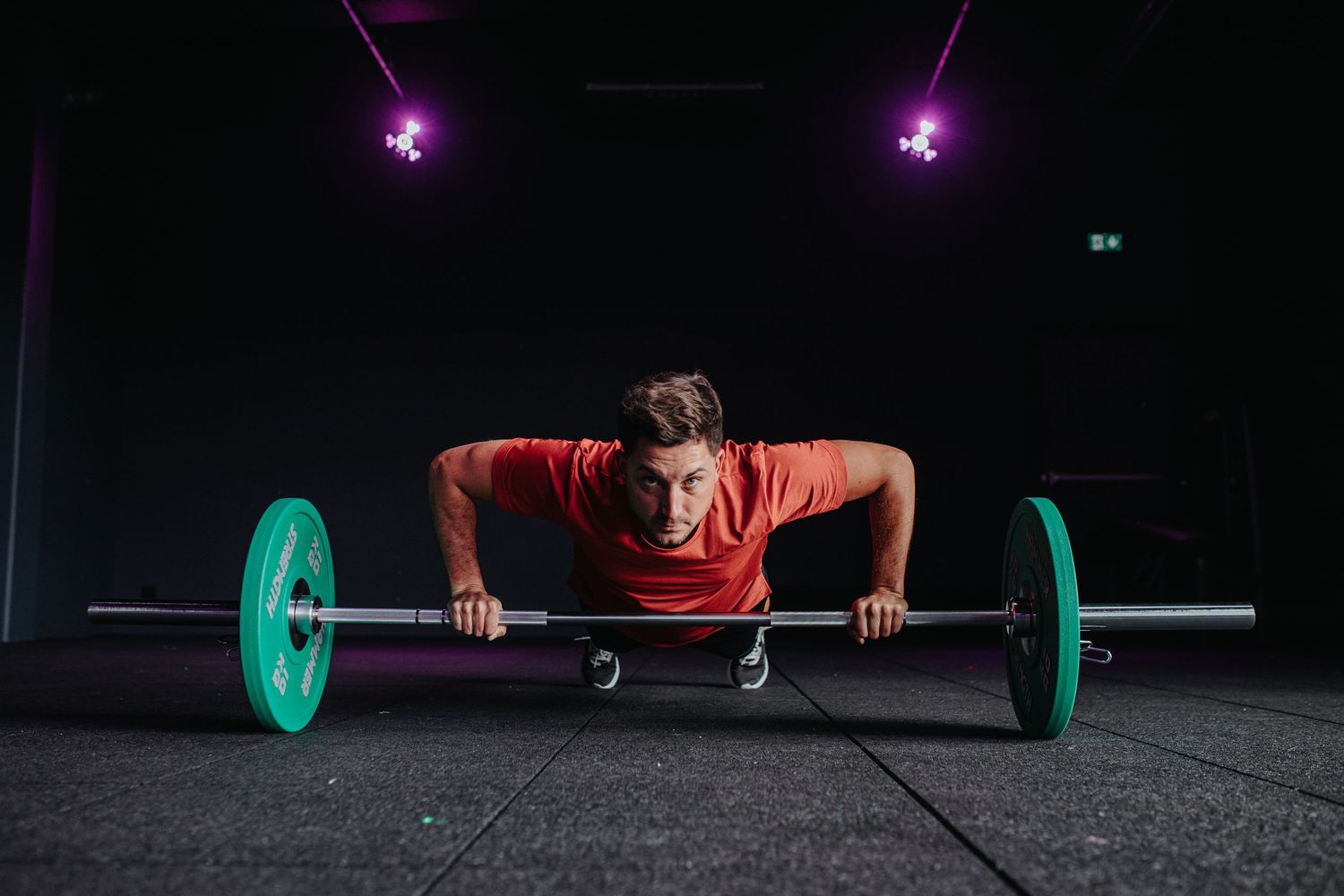 Four images showing a weightlifter performing a snatch sequence on a dark platform under purple lighting.