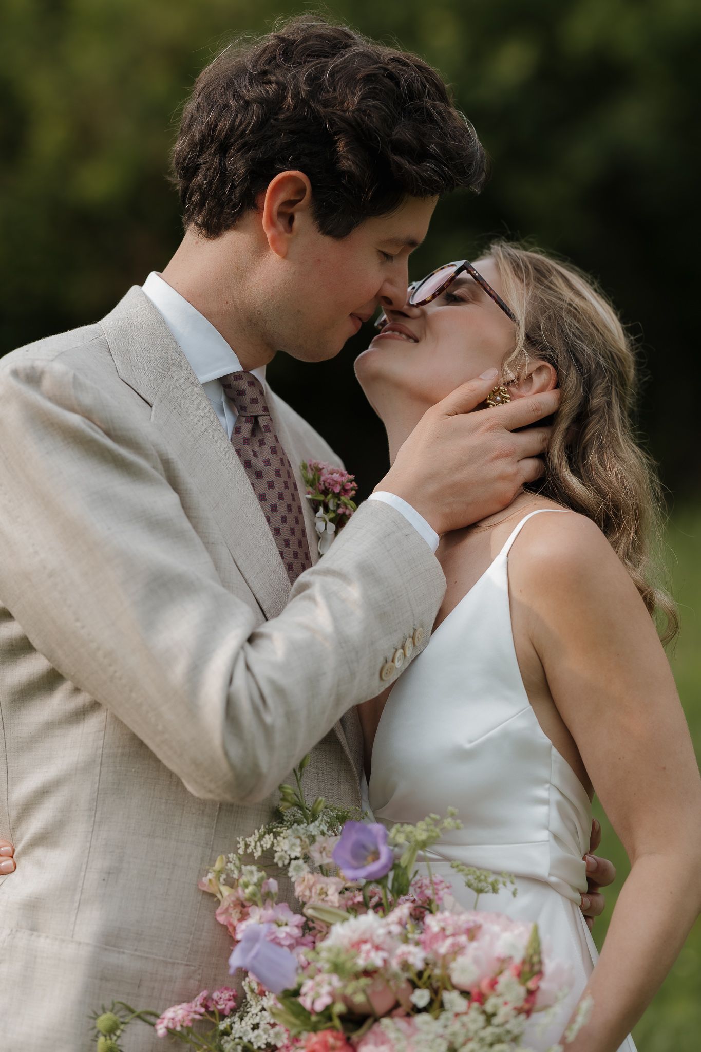 A romantic wedding moment with a couple sharing a tender kiss as they hold a pink and purple floral bouquet.