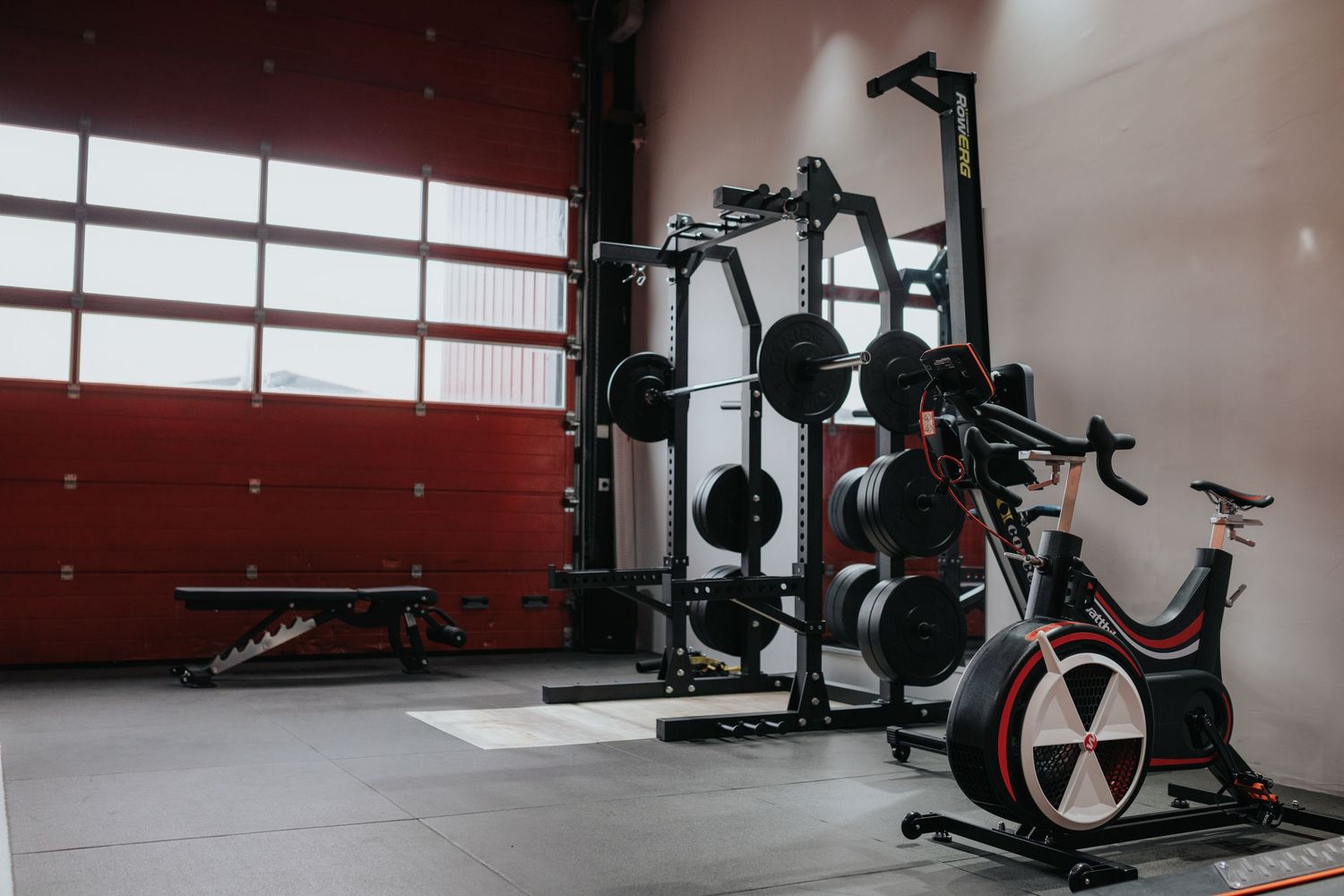 Private empty fitness studio equipped with a variety of workout machines lit by large windows along the wall.