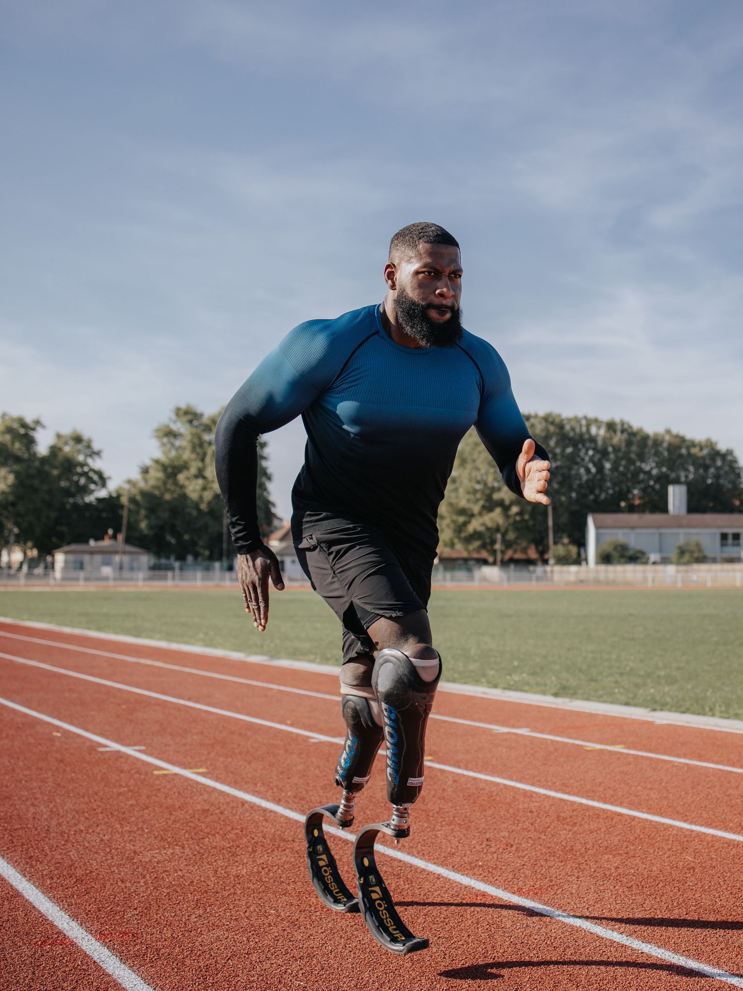 Athlete with prosthetic running blades trains on an outdoor track during cloudy weather.