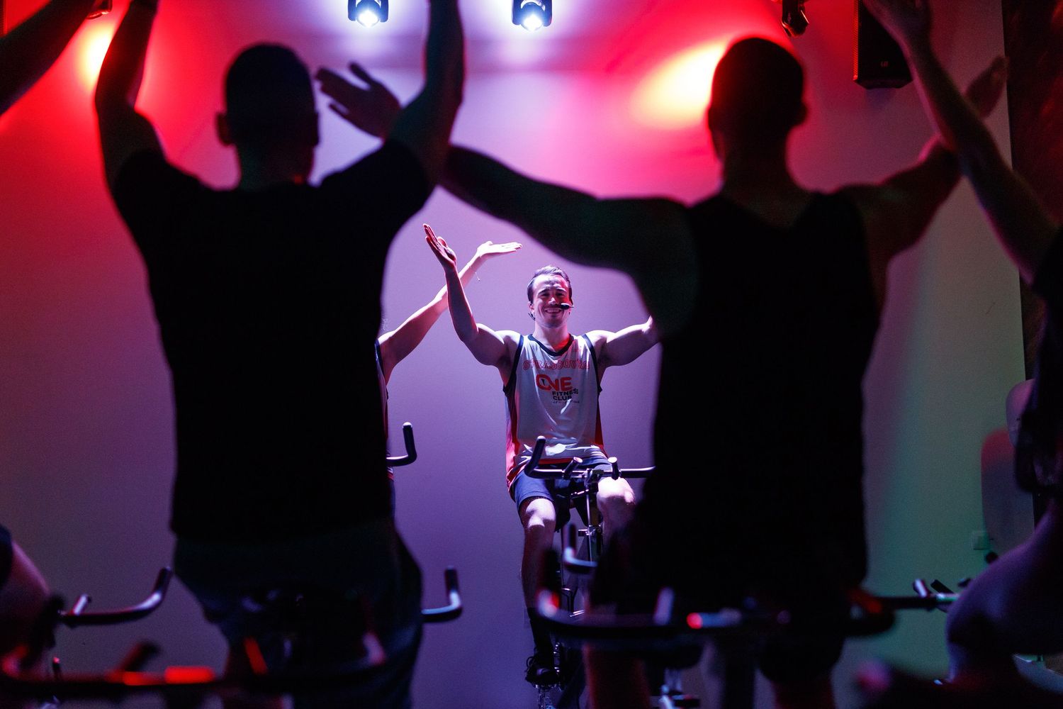 Silhouettes of people dancing with raised arms against colorful stage lighting and a drummer performing in the background.