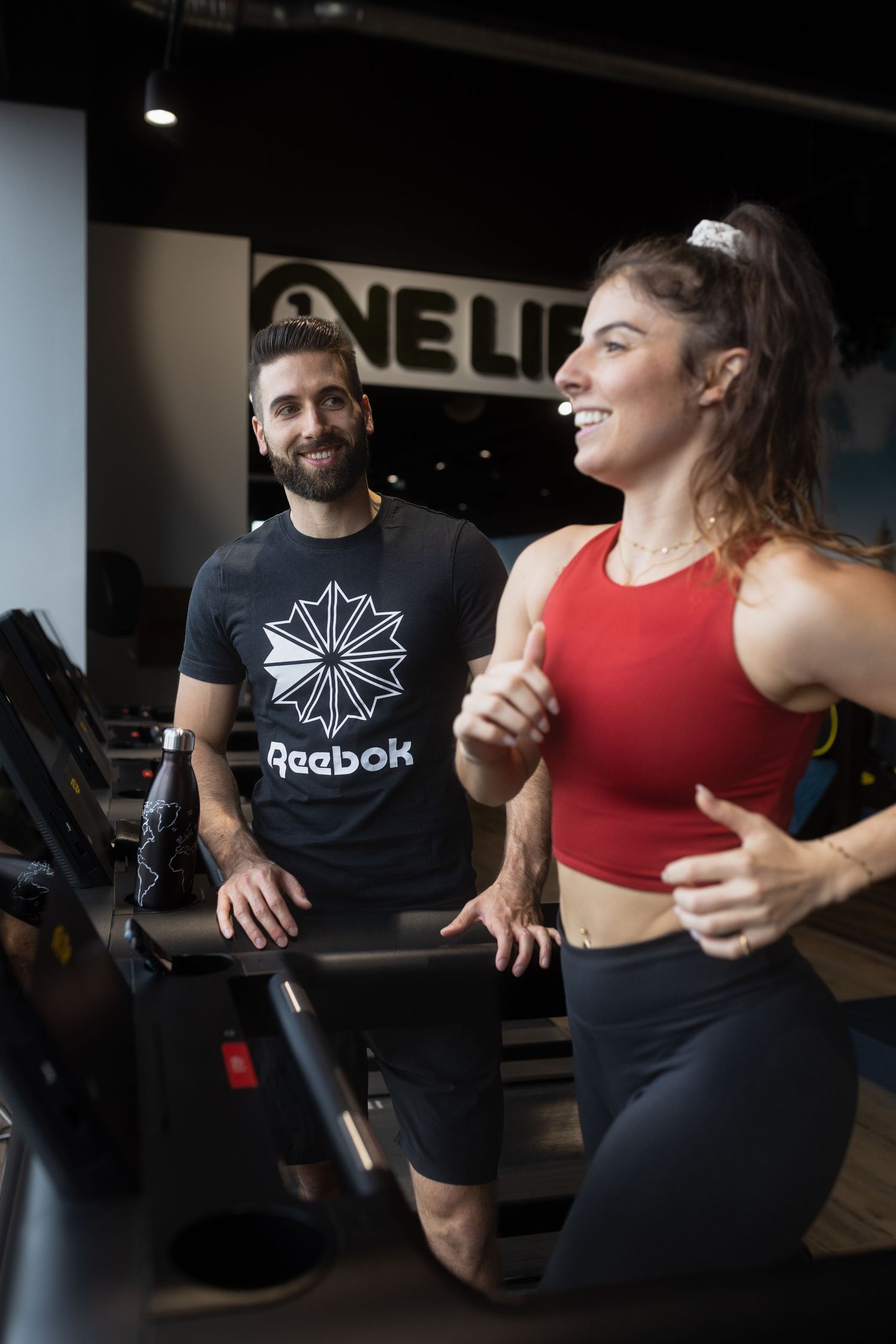 Two fitness enthusiasts engage in a lighthearted moment at the gym, wearing athletic attire during a workout session.