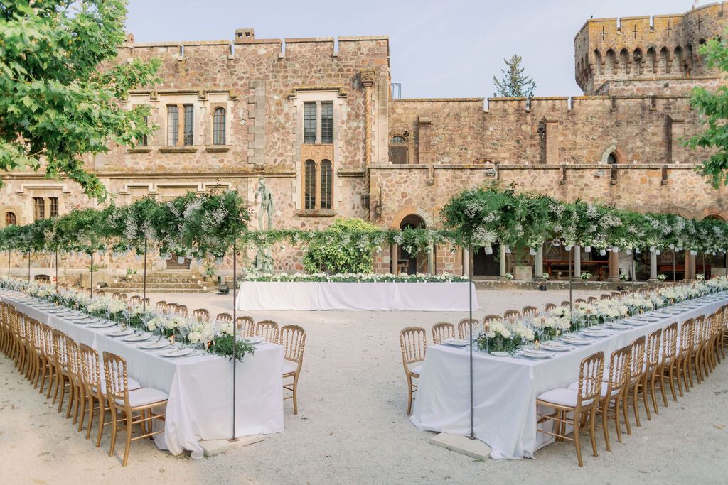 Elegant outdoor wedding reception setup with long tables and gold chairs at a historic stone castle venue.