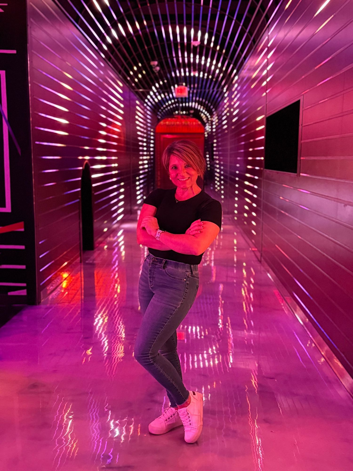 A figure poses in a futuristic corridor with pink lighting and lined with illuminated white bars creating a tunnel effect.