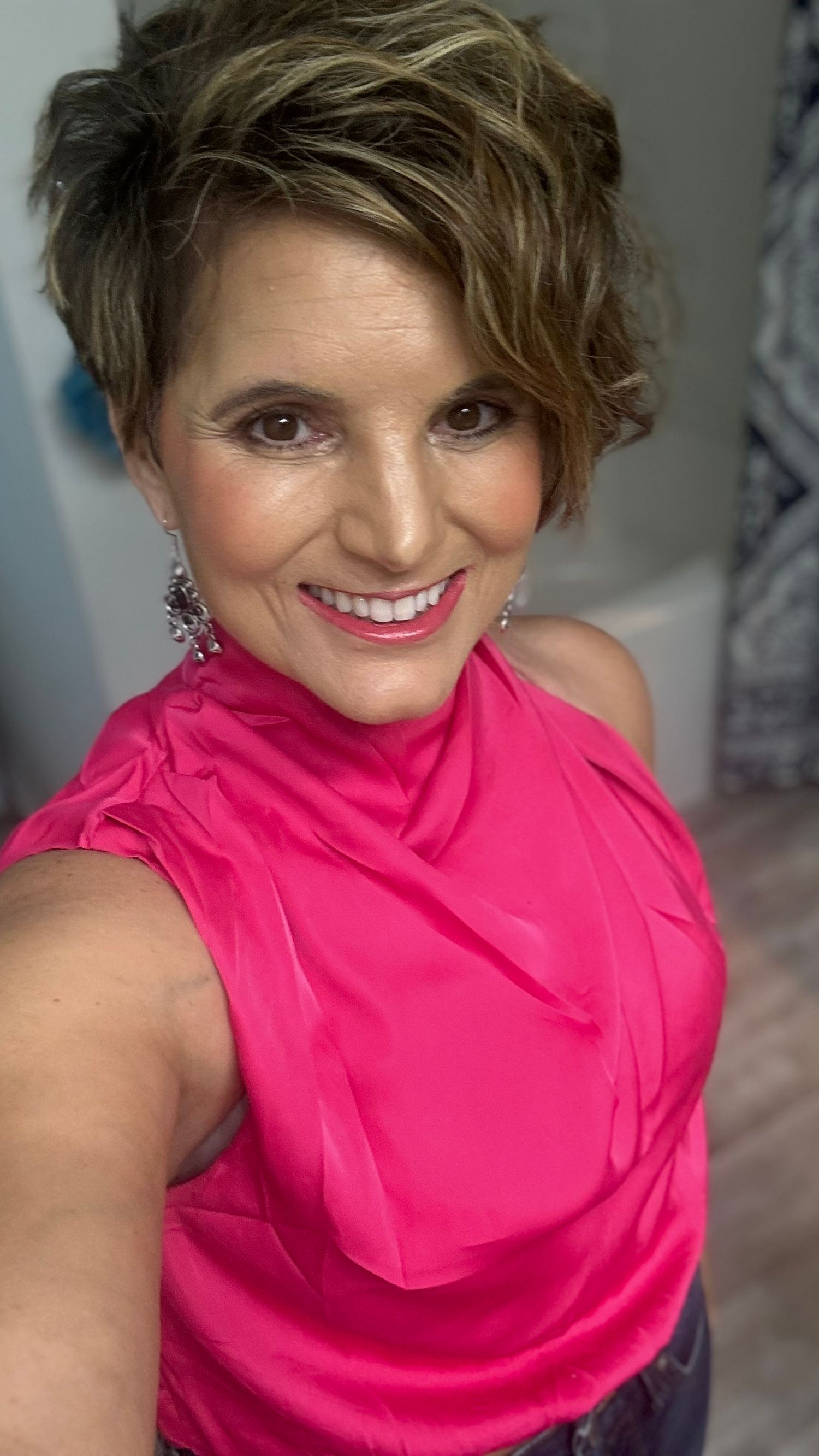 Glamorous selfie showing someone in a bright pink sleeveless top with styled hair and dangling earrings.
