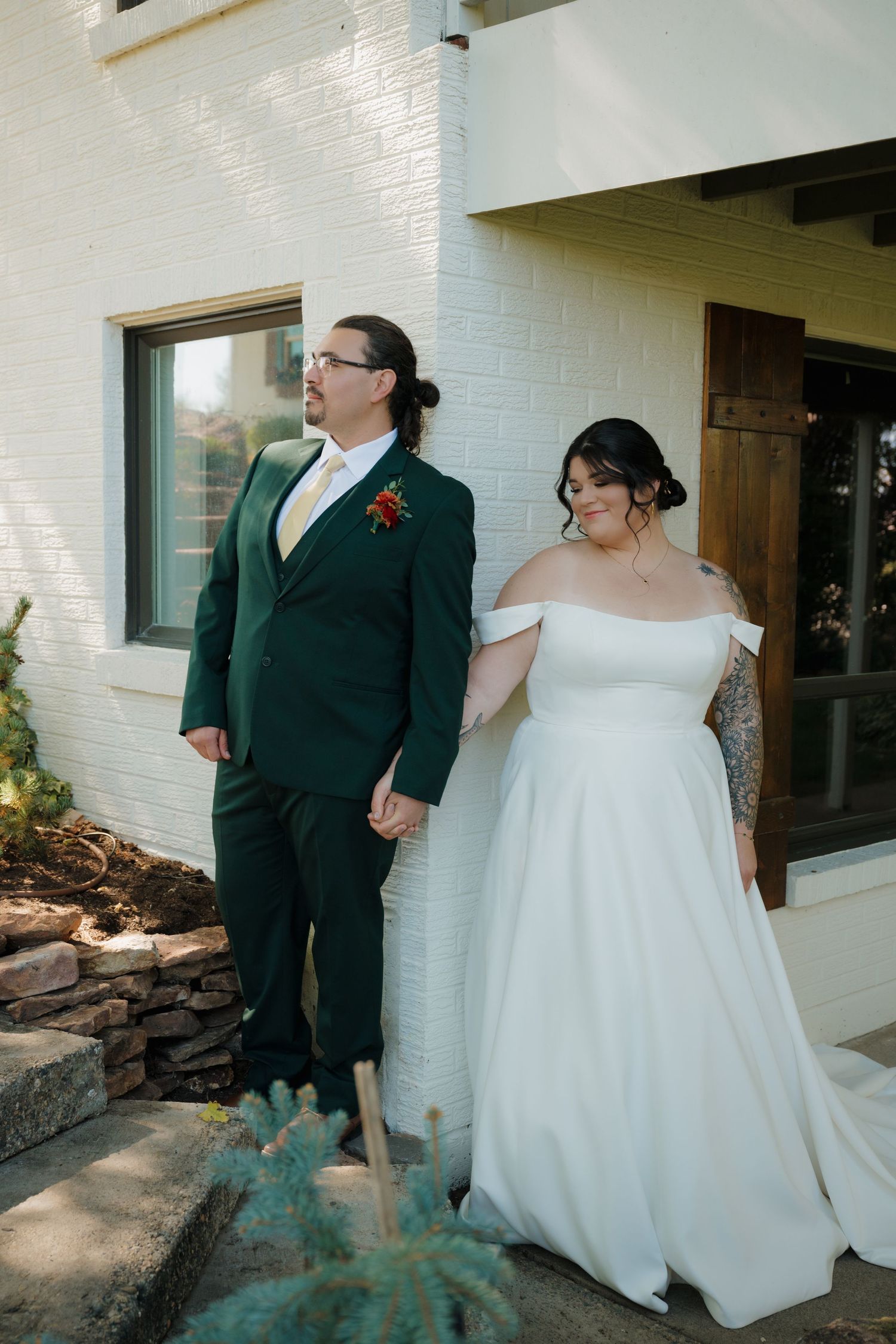 A couple poses outside a white brick building in formal wedding attire.