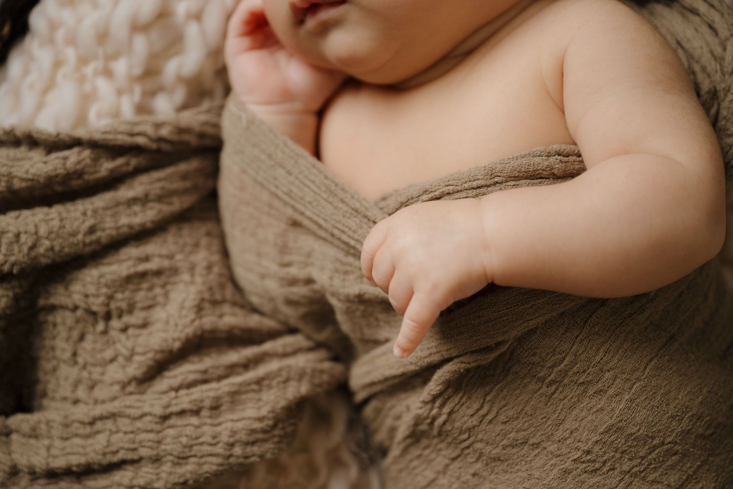 Close-up of baby's soft bare skin against textured brown fabric.