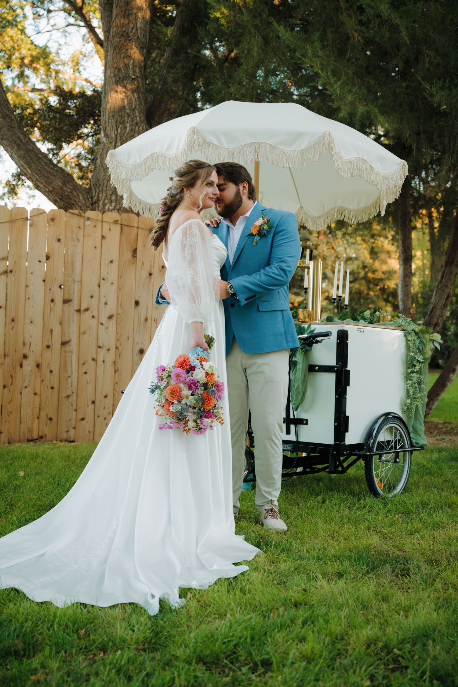 A couple shares a romantic moment under a white parasol with a vintage cart in the background.