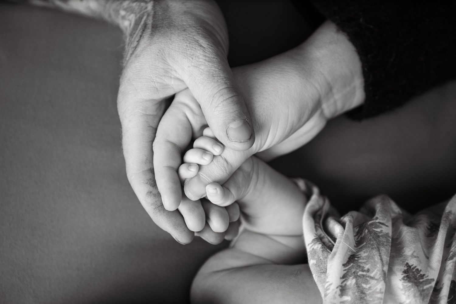 Black and white image of adult hands tenderly holding baby's tiny feet.