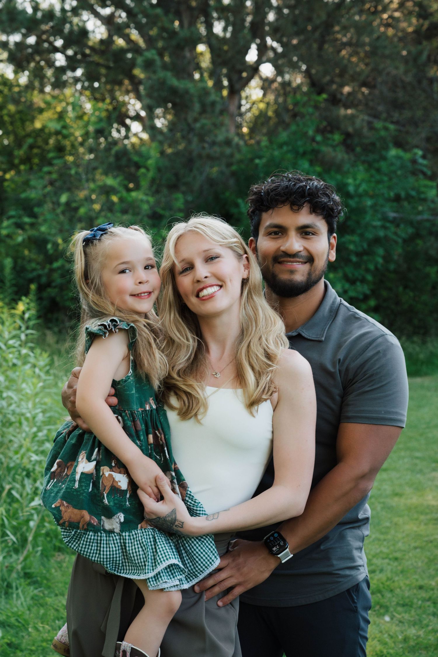 A family in coordinated outfits shares joyful moments together during an outdoor photo session in a green park setting.