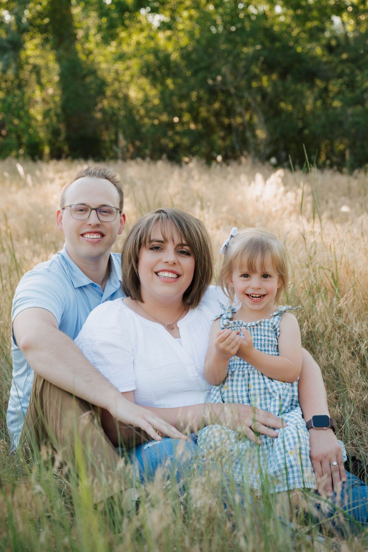 A family sits together in a sun-lit field of tall grass during a warm summer evening photo session.