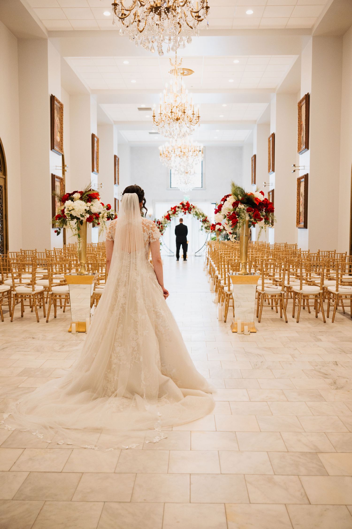 Wedding ceremony venue with gold chairs, floral arrangements, and chandeliers.