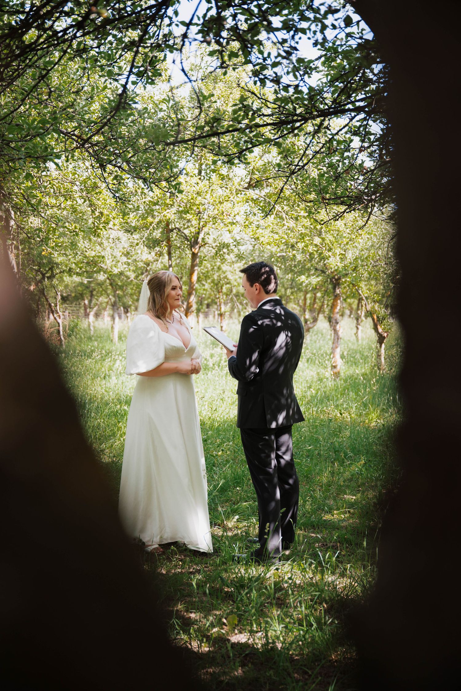 A couple shares an intimate moment in a sun-dappled forest clearing during their wedding photoshoot.